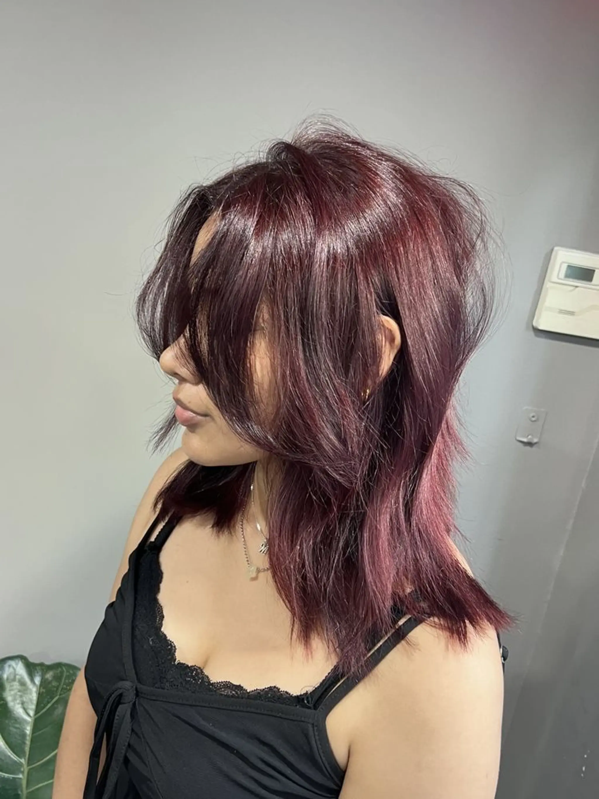 A medium-length, straight hairstyle with deep red and dark burgundy hues, featuring choppy layers and textured, jagged bangs.