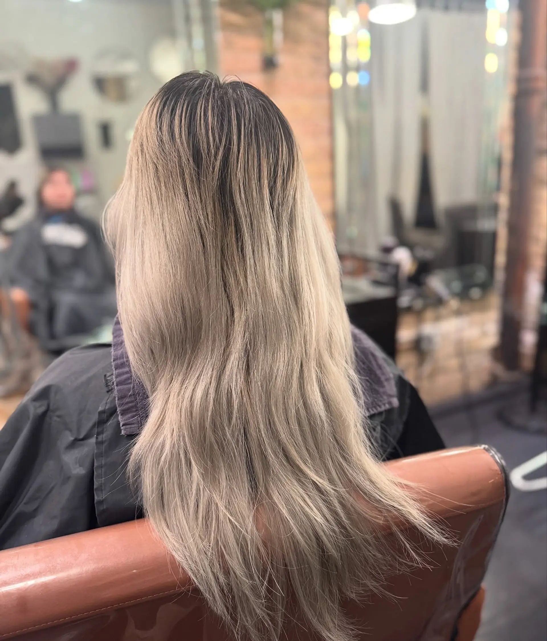 Long ash blonde hair with a deep brunette root blend seamlessly transitioning into cool, brightened ends. 1