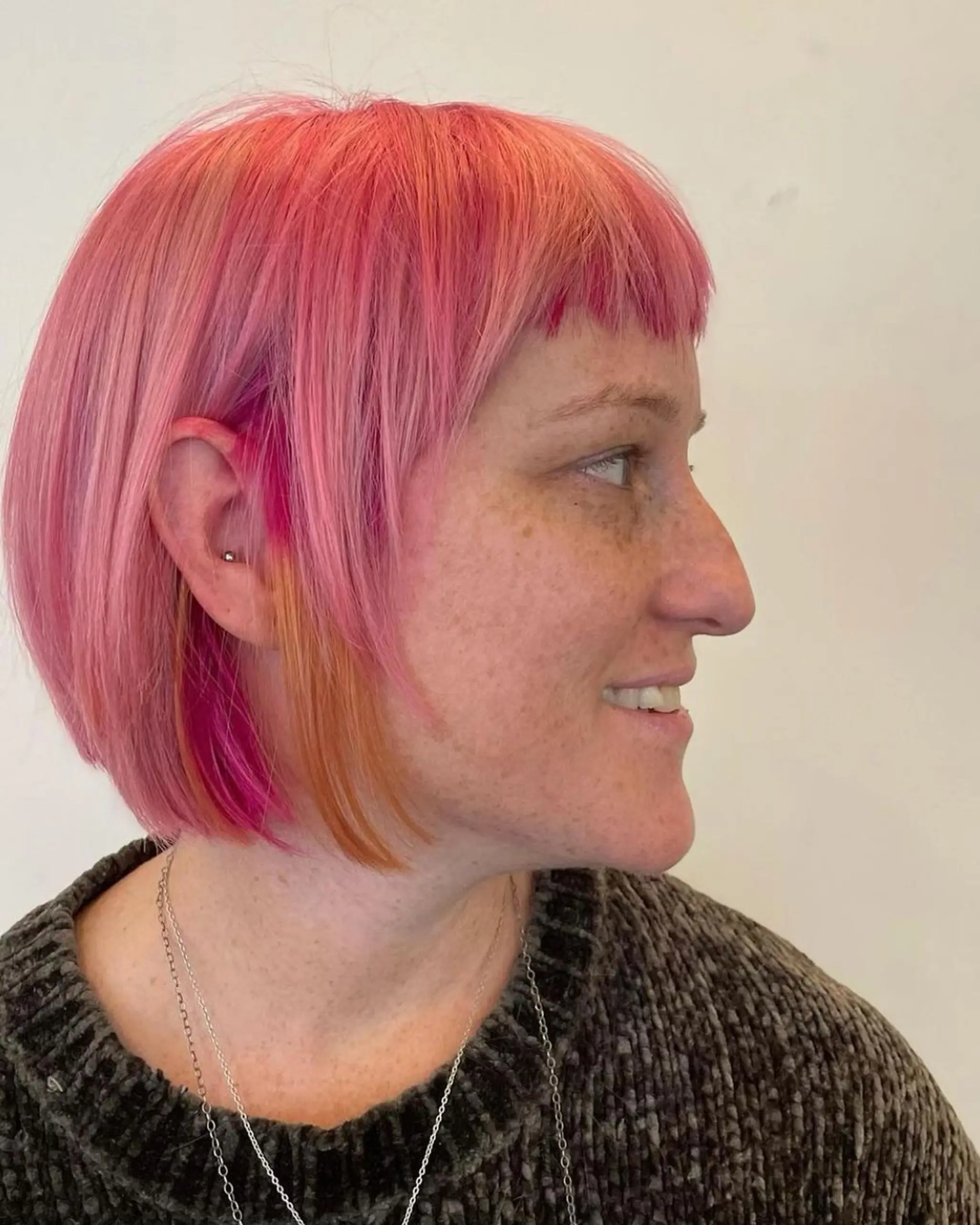 A vibrant short bob with blunt bangs, featuring pink and orange hues in a straight, layered style.