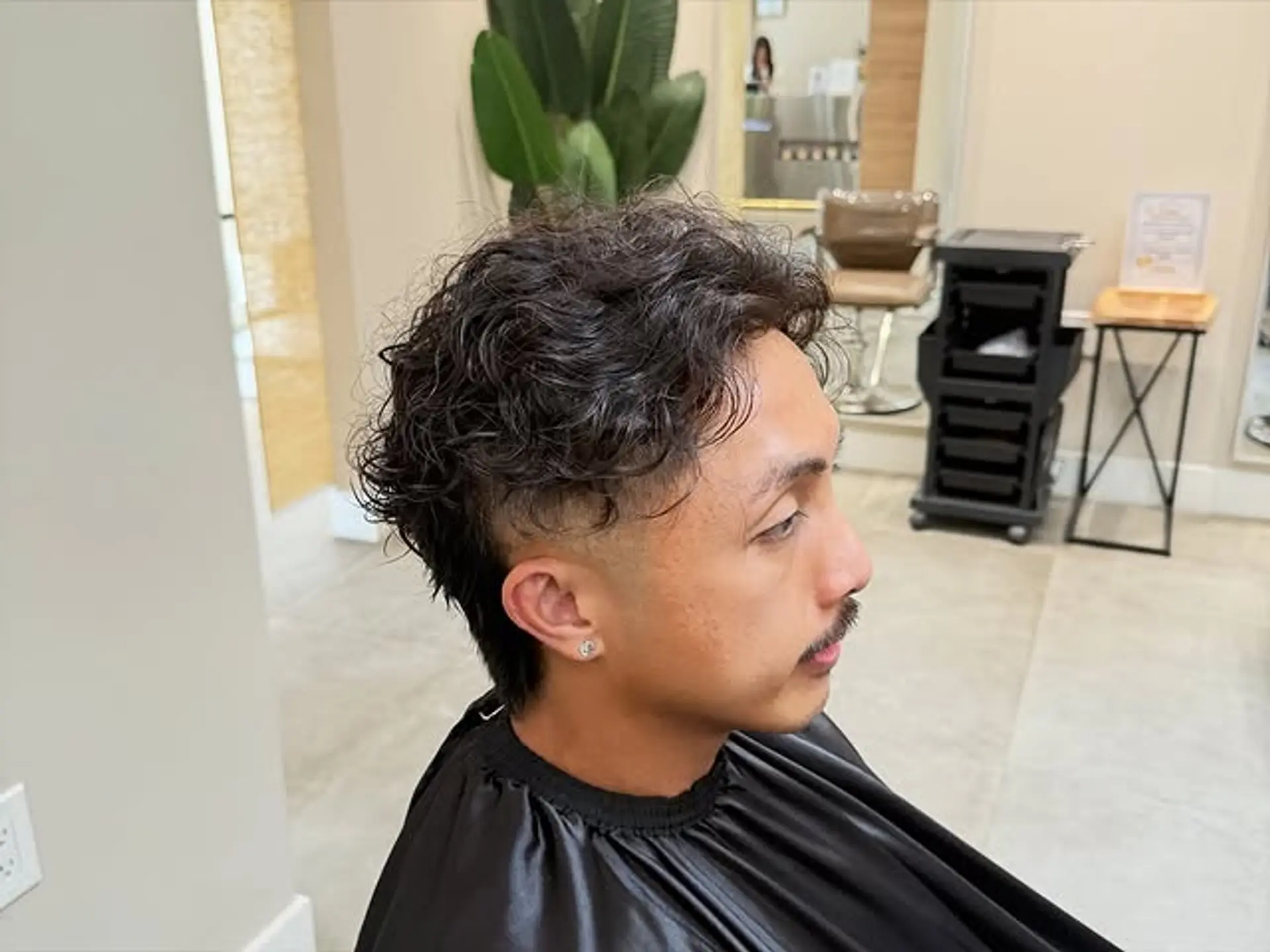 A contemporary mullet featuring textured curls on top and a clean fade on the sides. 1