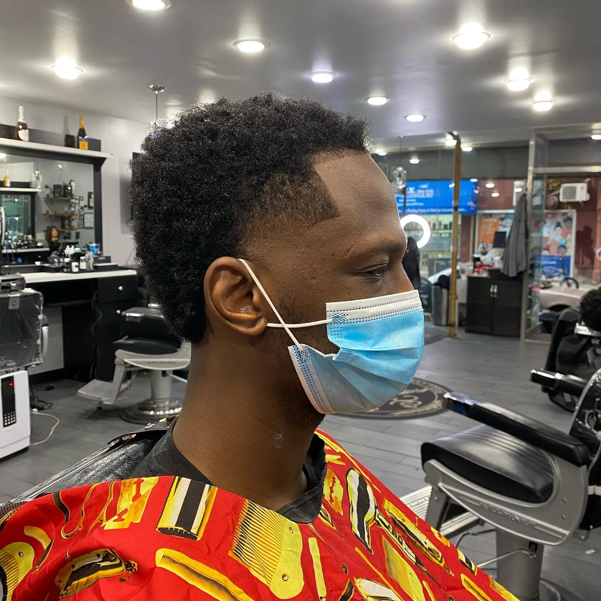 A short coily haircut featuring a clean temple taper fade, crisp hairline shape-up, and textured natural volume on top. 1