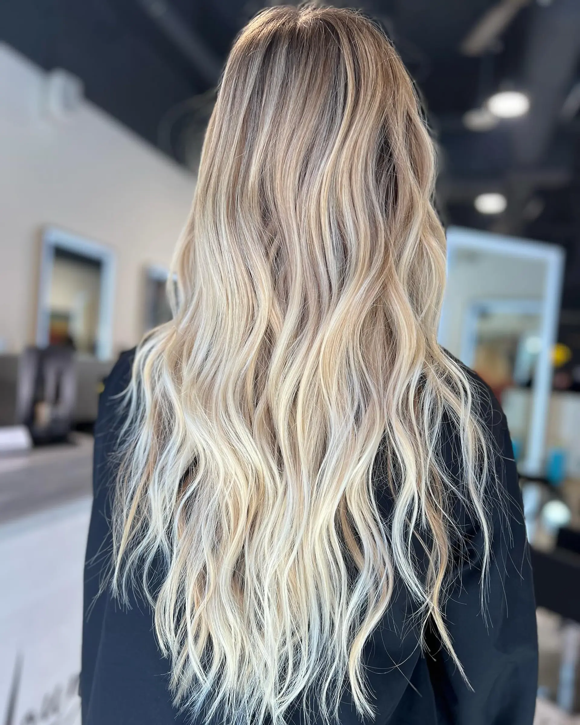 Very long, dimensional blonde hair styled into soft, beachy waves with a lived-in root blend. 1