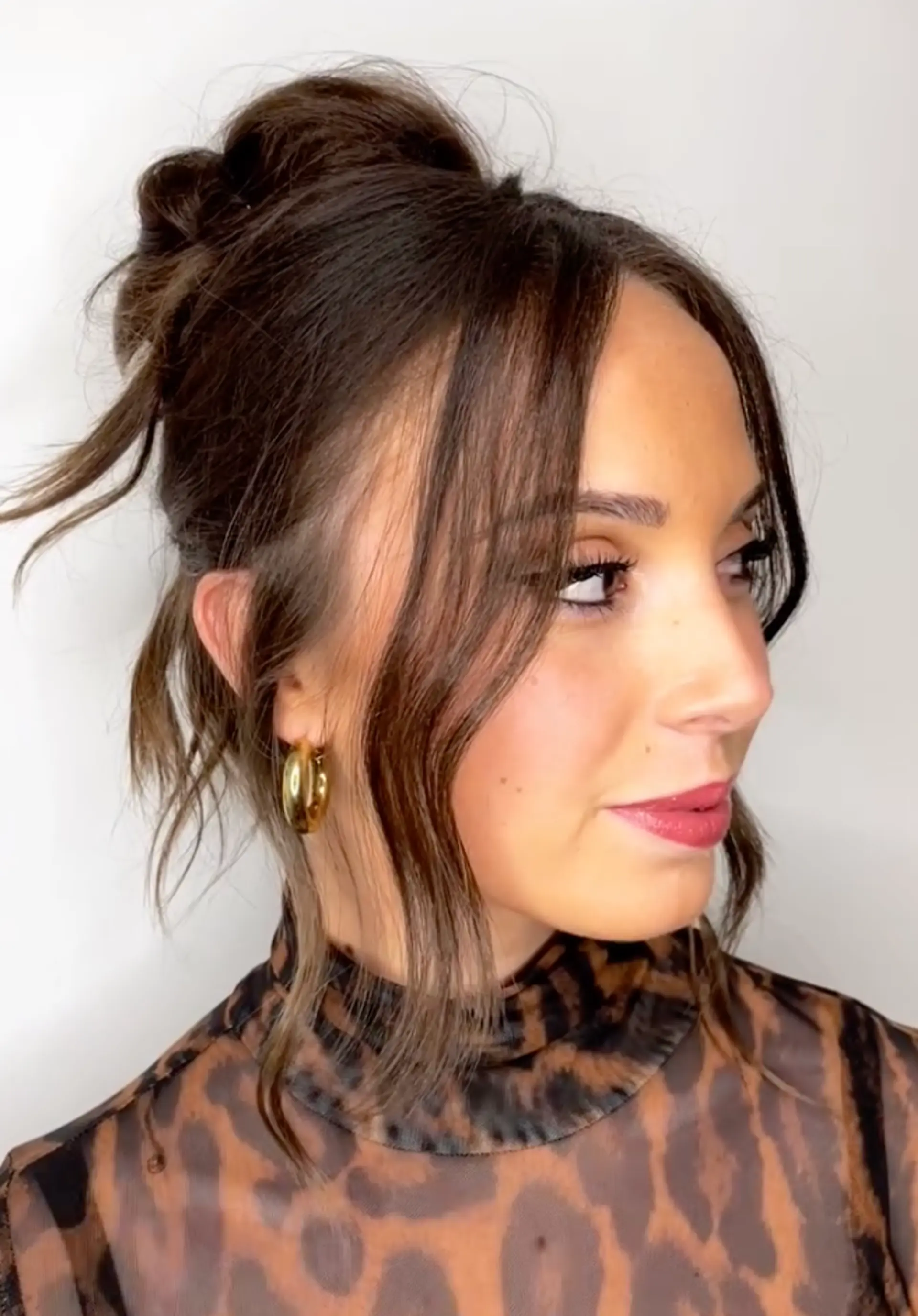 An elegant tousled updo with medium-length brunette hair. Features a chic loose bun with wavy strands and wispy bangs framing the face. Enhanced with gold hoop earrings.

Style by @juliamannino_hair 1