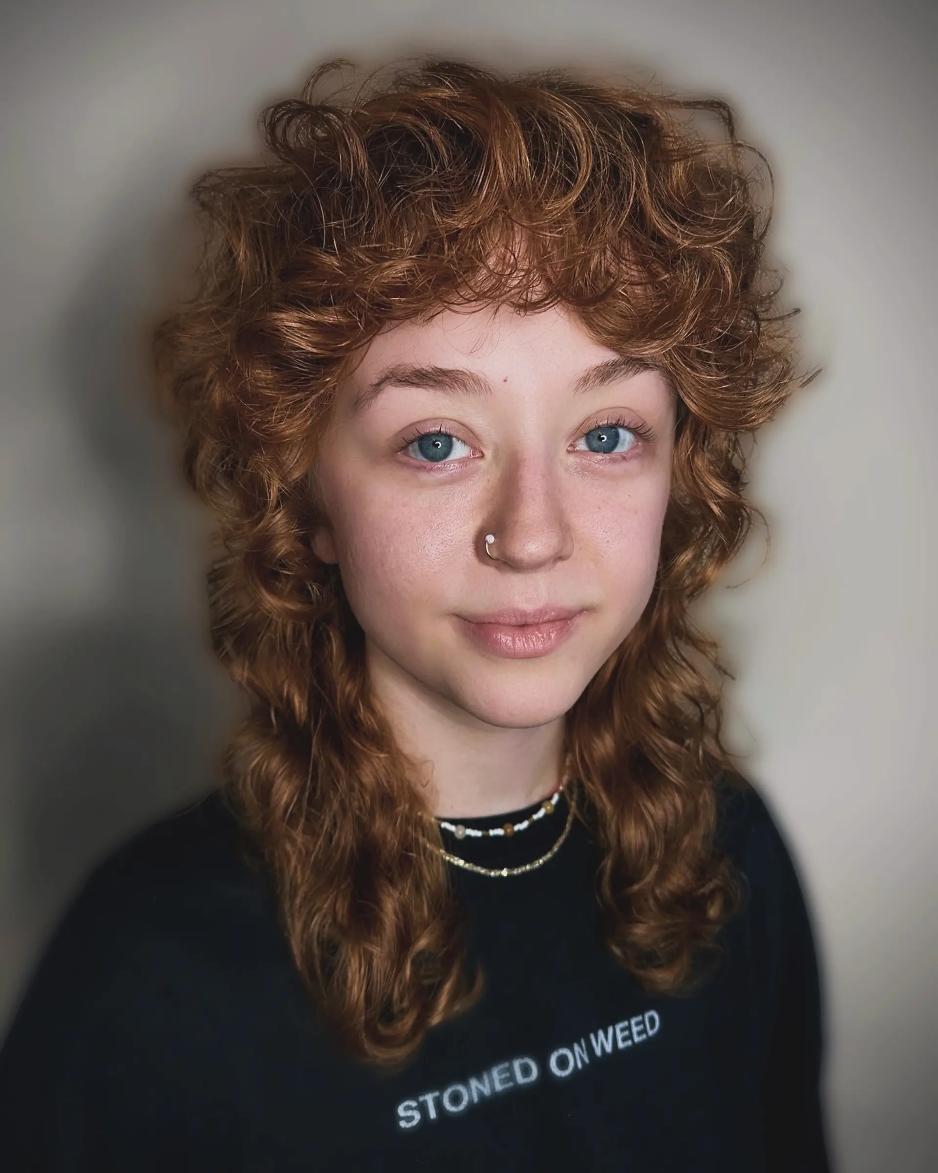 A textured copper curly shullet featuring full curly bangs, voluminous face-framing layers, and longer curly lengths falling toward the shoulders. 1