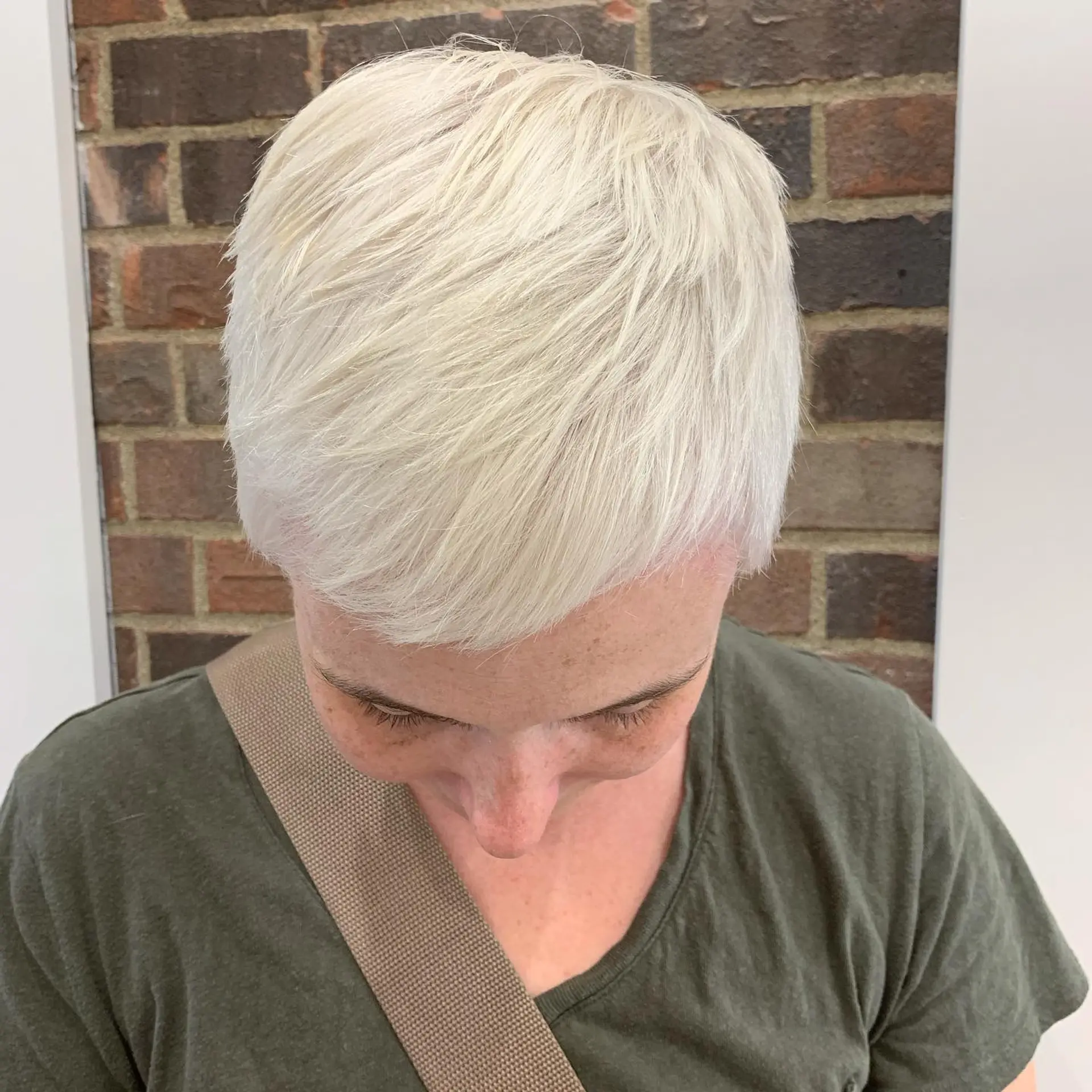 A textured short pixie cut styled forward with soft fringe, lightened to an icy, solid platinum blonde. 1