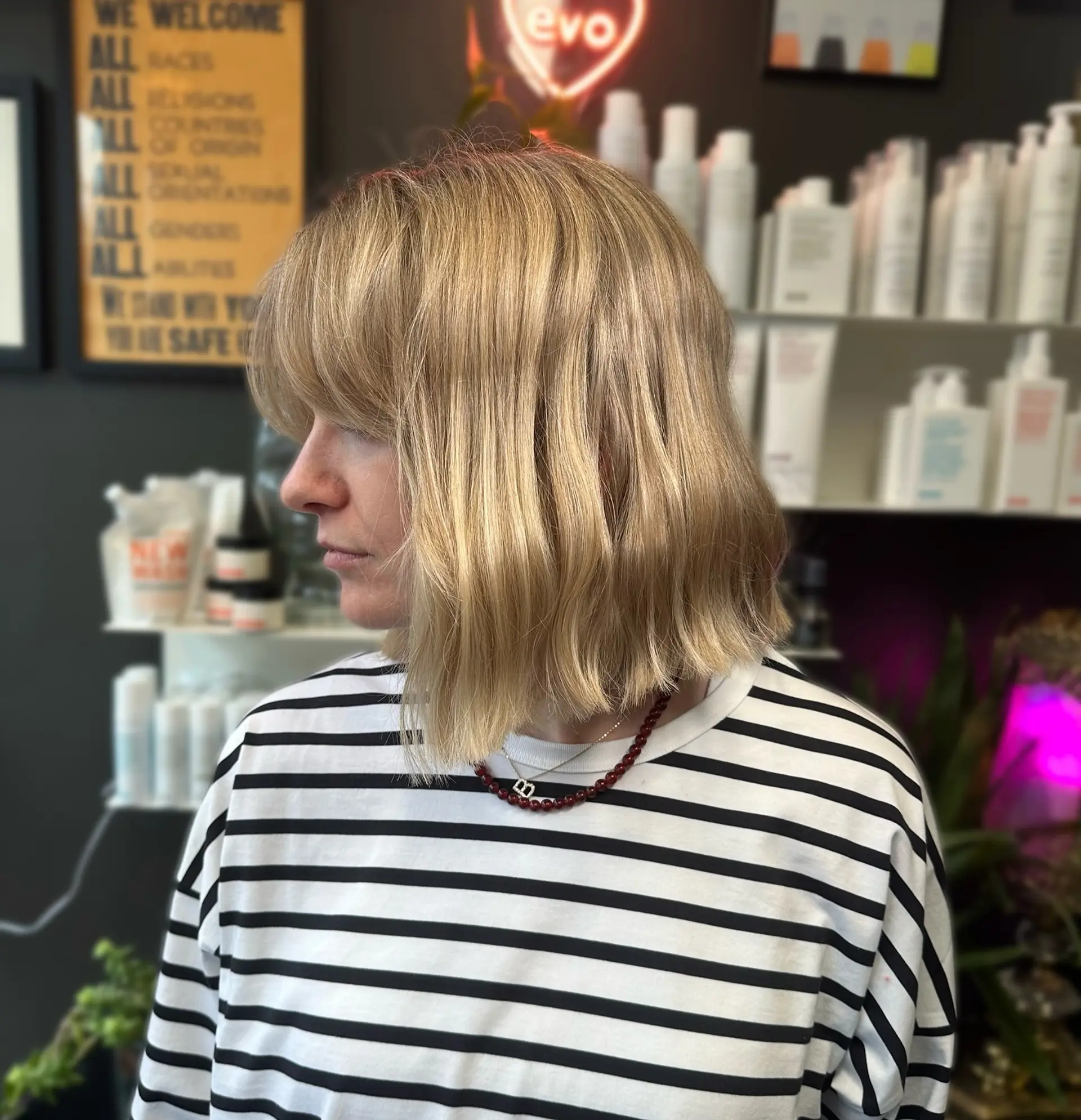A chic short bob cut with subtle wave texture, full rounded bangs, and multi-tonal warm blonde coloring. 1