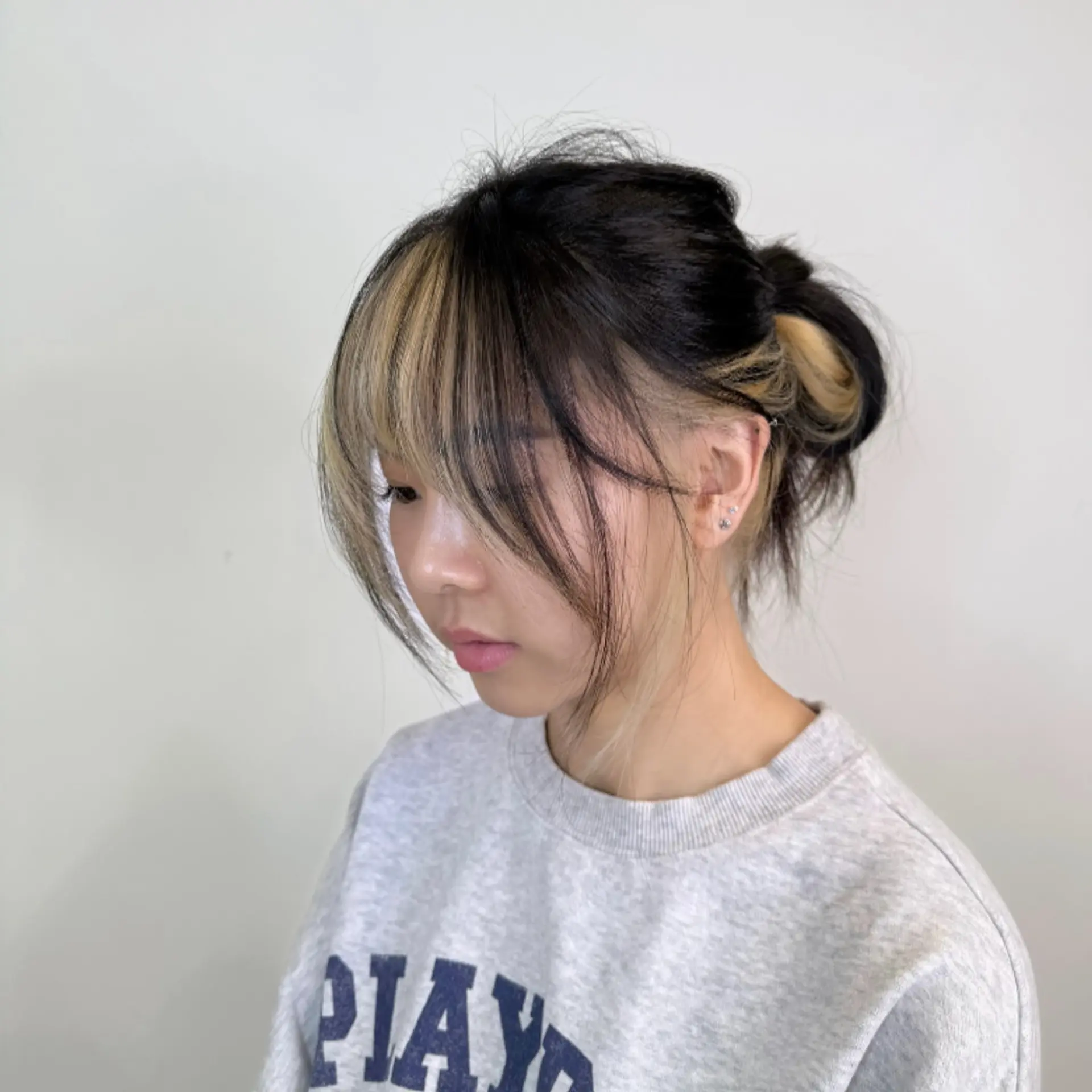 Casual updo showcasing contrasting pale blonde money piece highlights integrated into wispy bangs and face-framing strands. 1