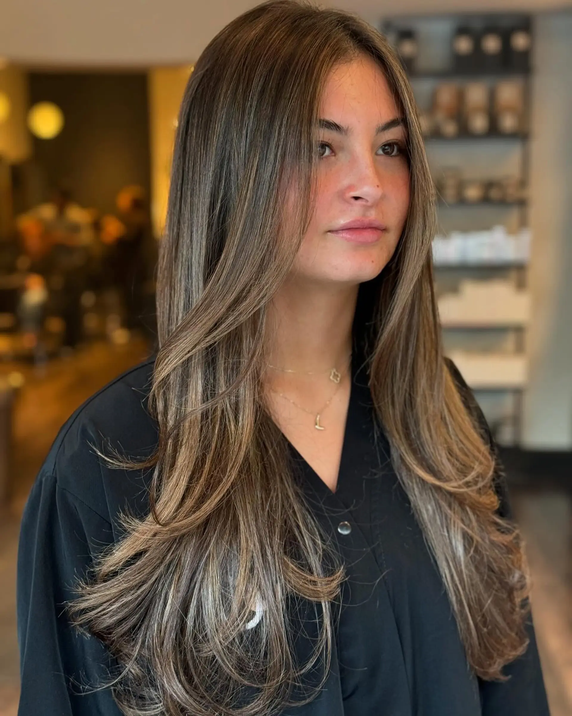 Long ash brunette hair cut with soft face-framing layers and styled into a sleek blowout with turned-under ends. 1