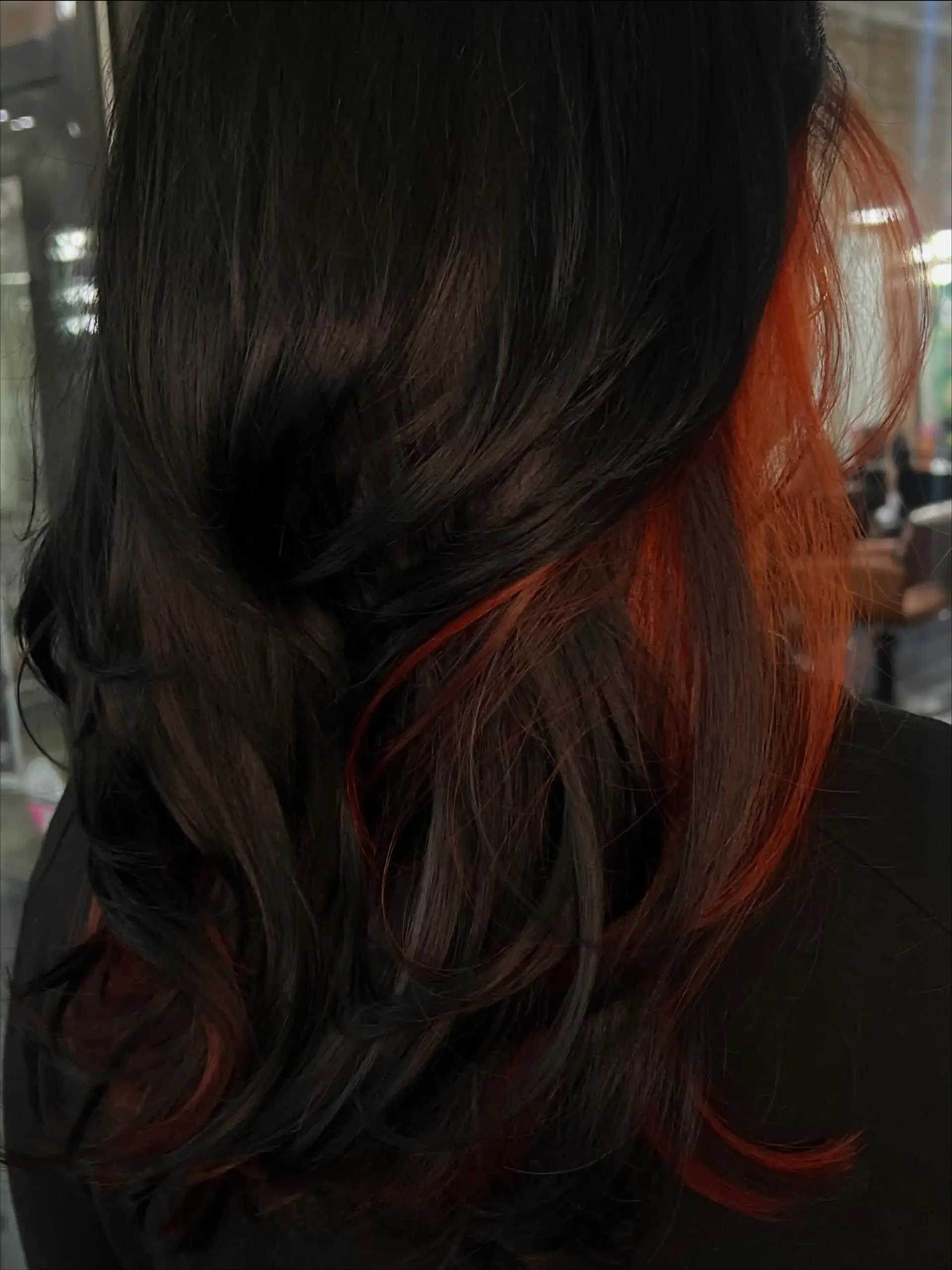 Long, flowing dark brown hair styled in soft waves with contrasting bright orange peekaboo color layered beneath. 1