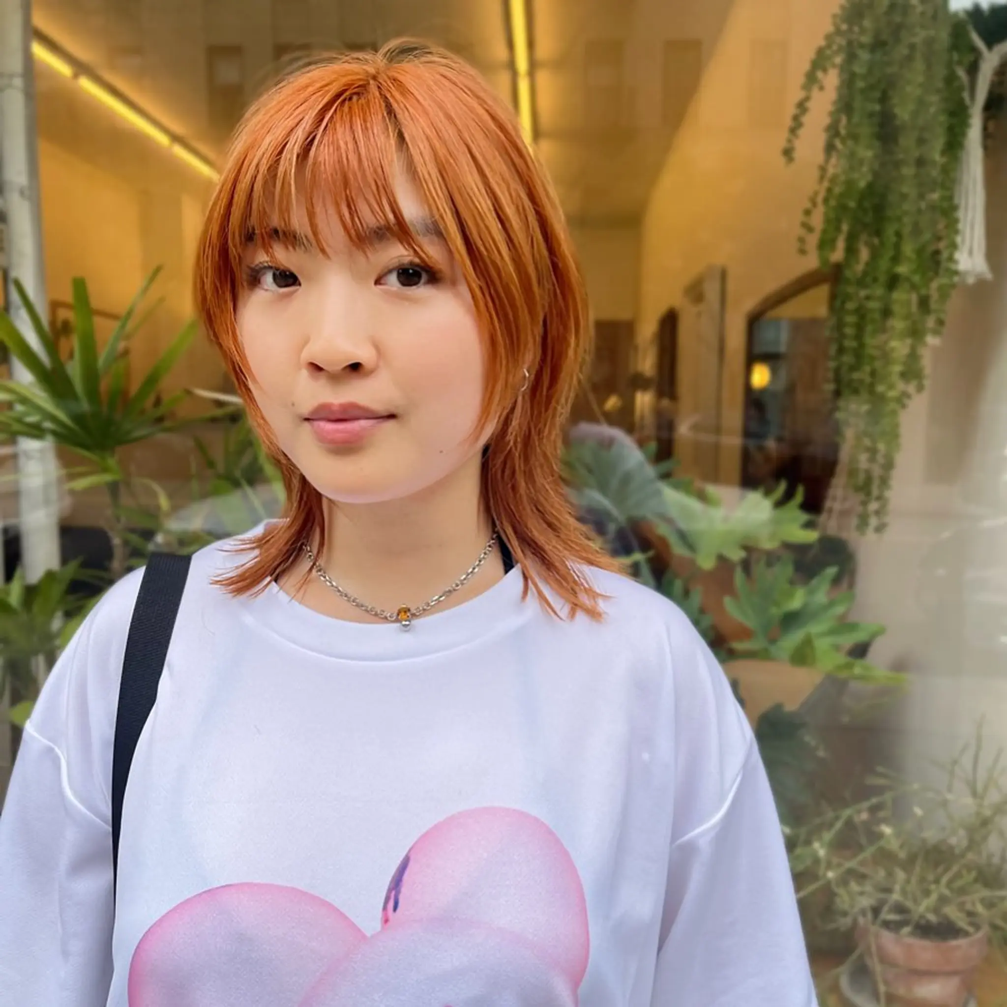 This medium-length, straight hairstyle features vibrant copper-orange tones with choppy layers and fringe bangs, ending in textured tips for a dynamic look.