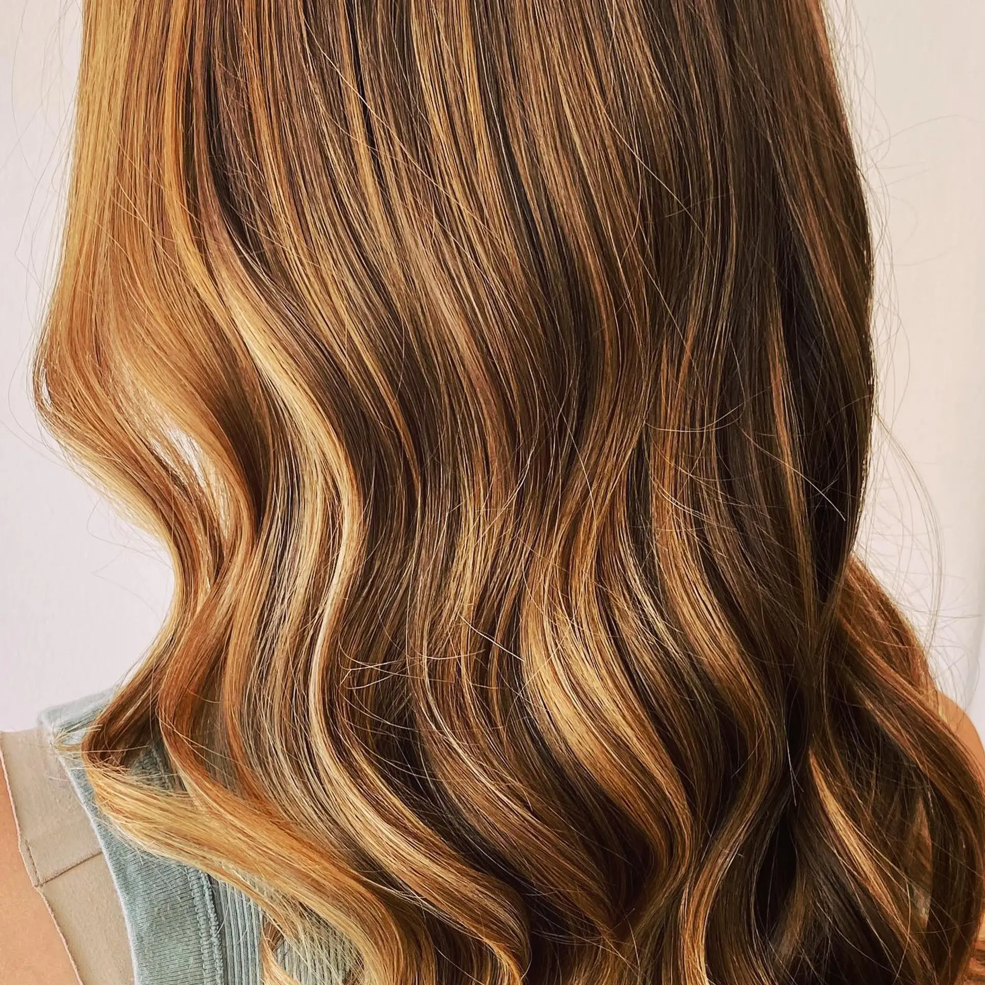 Long wavy brunette hair highlighted with warm caramel and golden tones in a blended balayage technique. 1