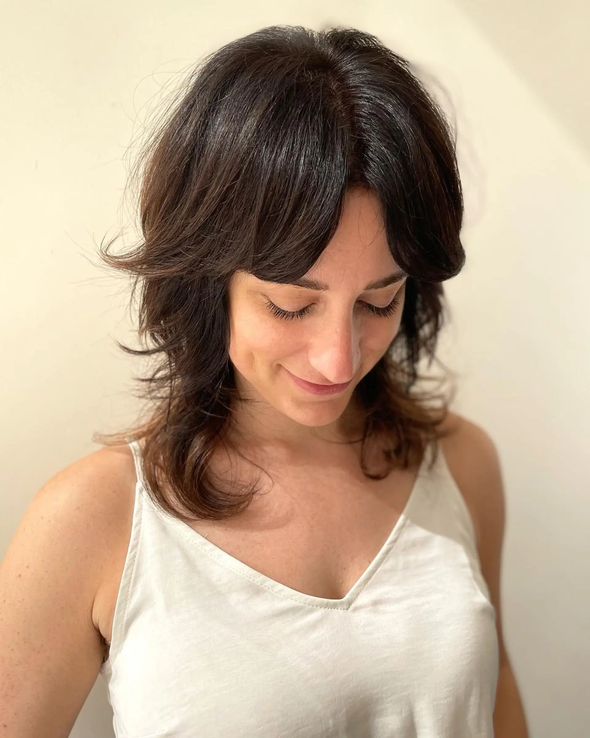 Medium-length dark brown wavy hair with feathered layers and side-swept bangs for a soft, natural look. 1