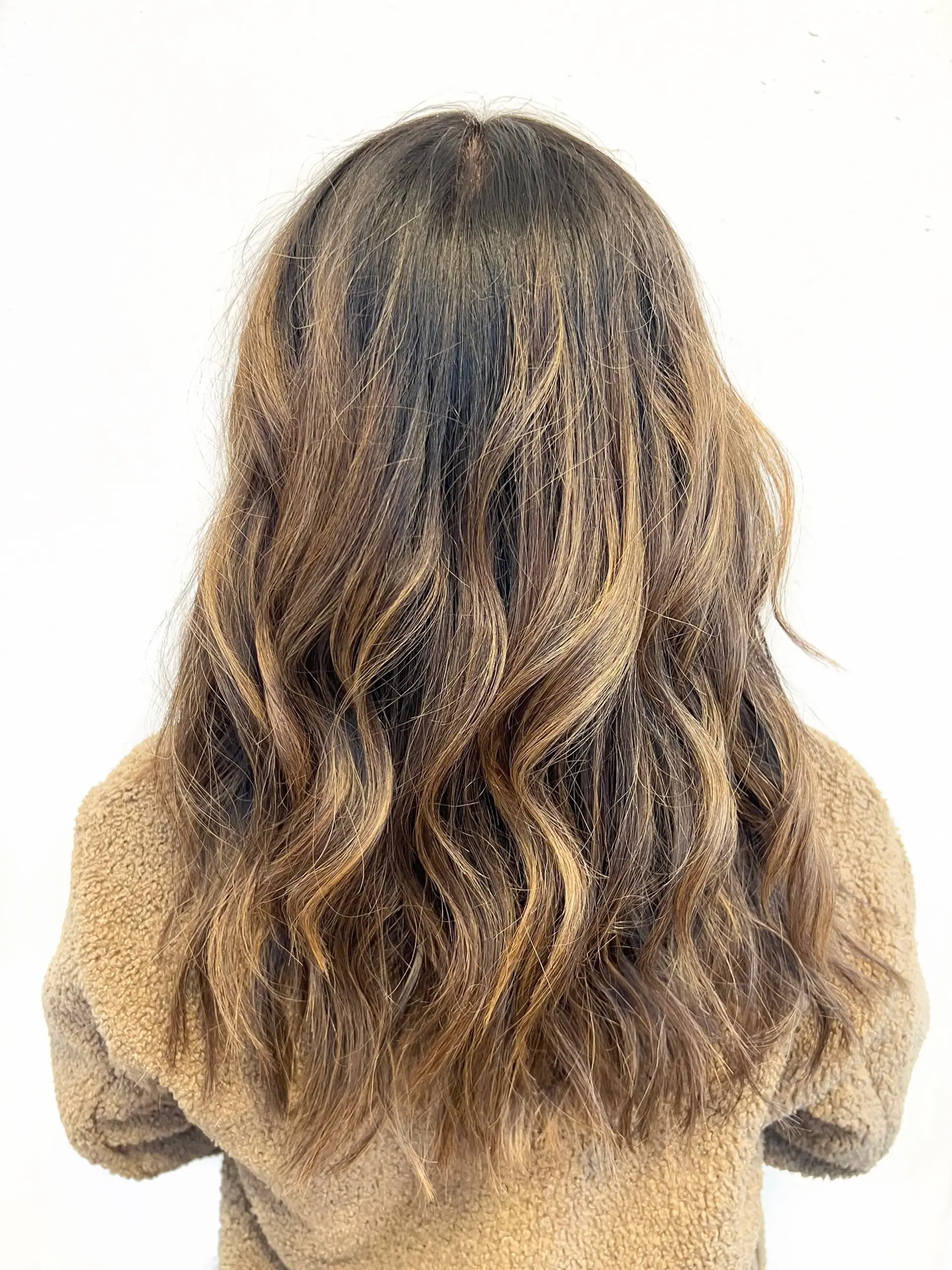 Long dimensional brunette hair with soft caramel balayage highlights styled in loose, textured waves. 1