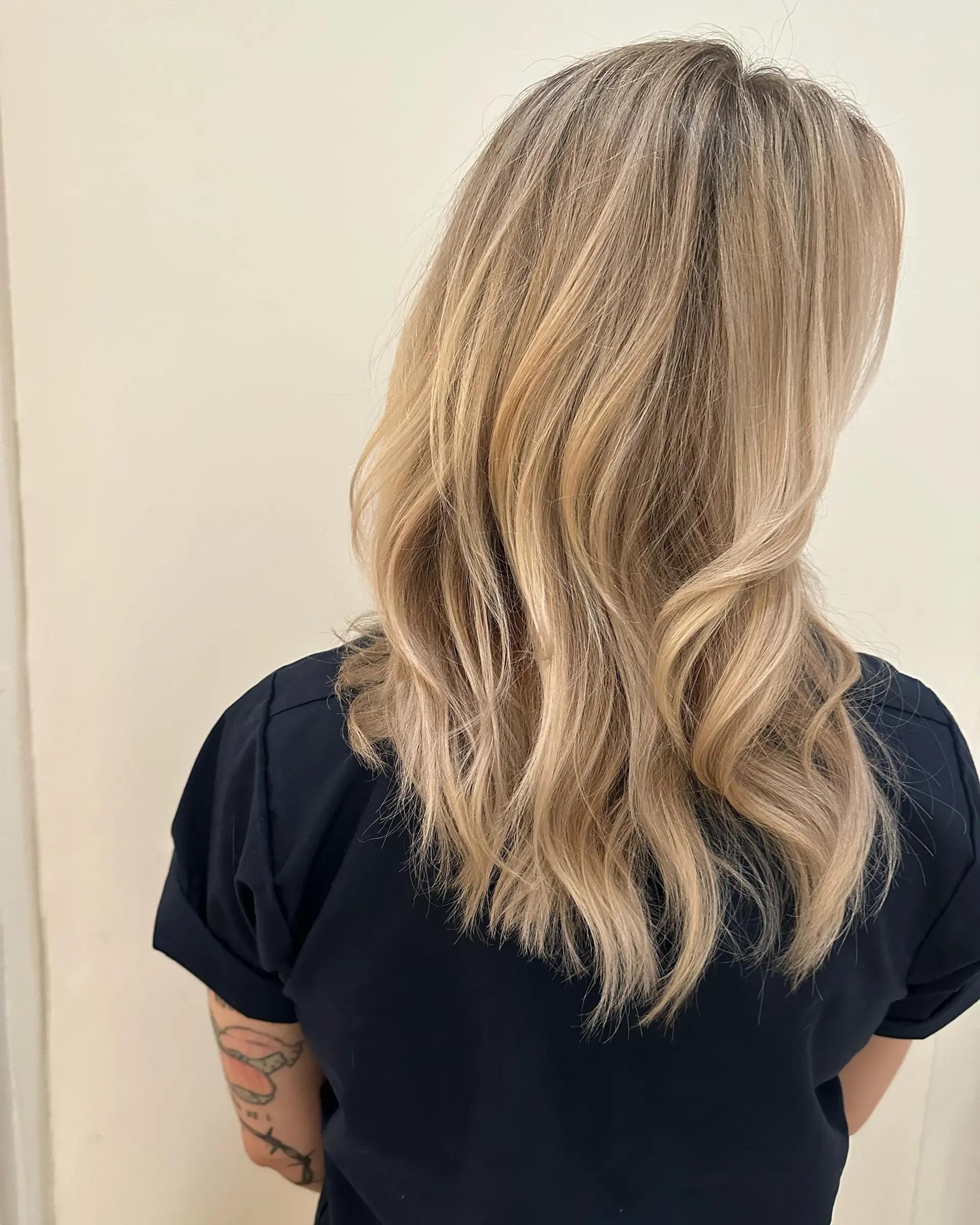 Dimensional neutral blonde hair cut in long layers and styled into gentle loose waves. 1