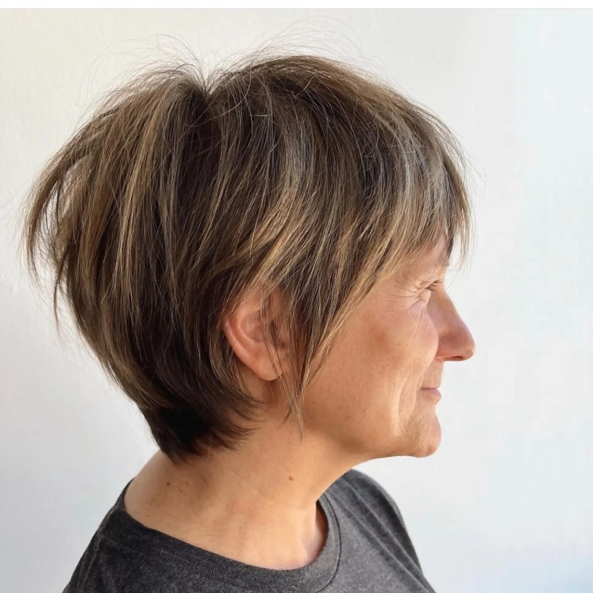 A side profile showing a textured pixie bob with soft layering, volume at the crown, and piecey pieces framing the cheek and ear. 1