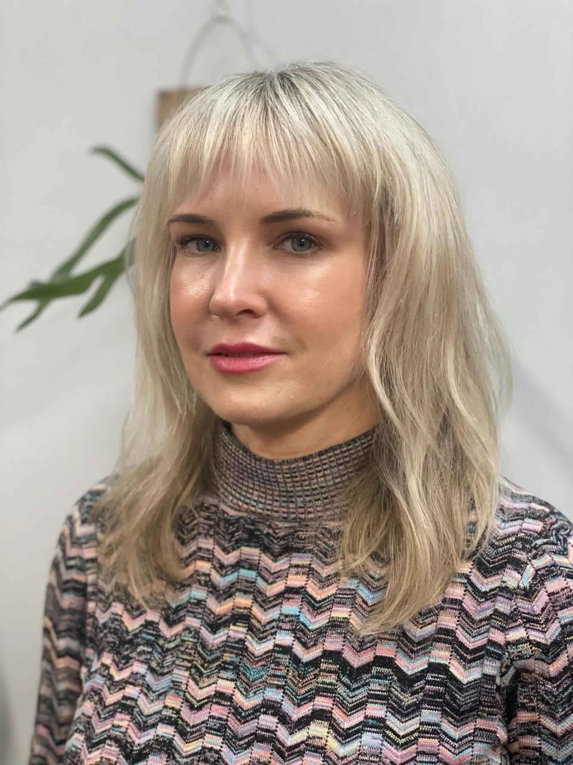 A medium-length pearl blonde haircut with soft wispy bangs and gentle, textured layering. 1