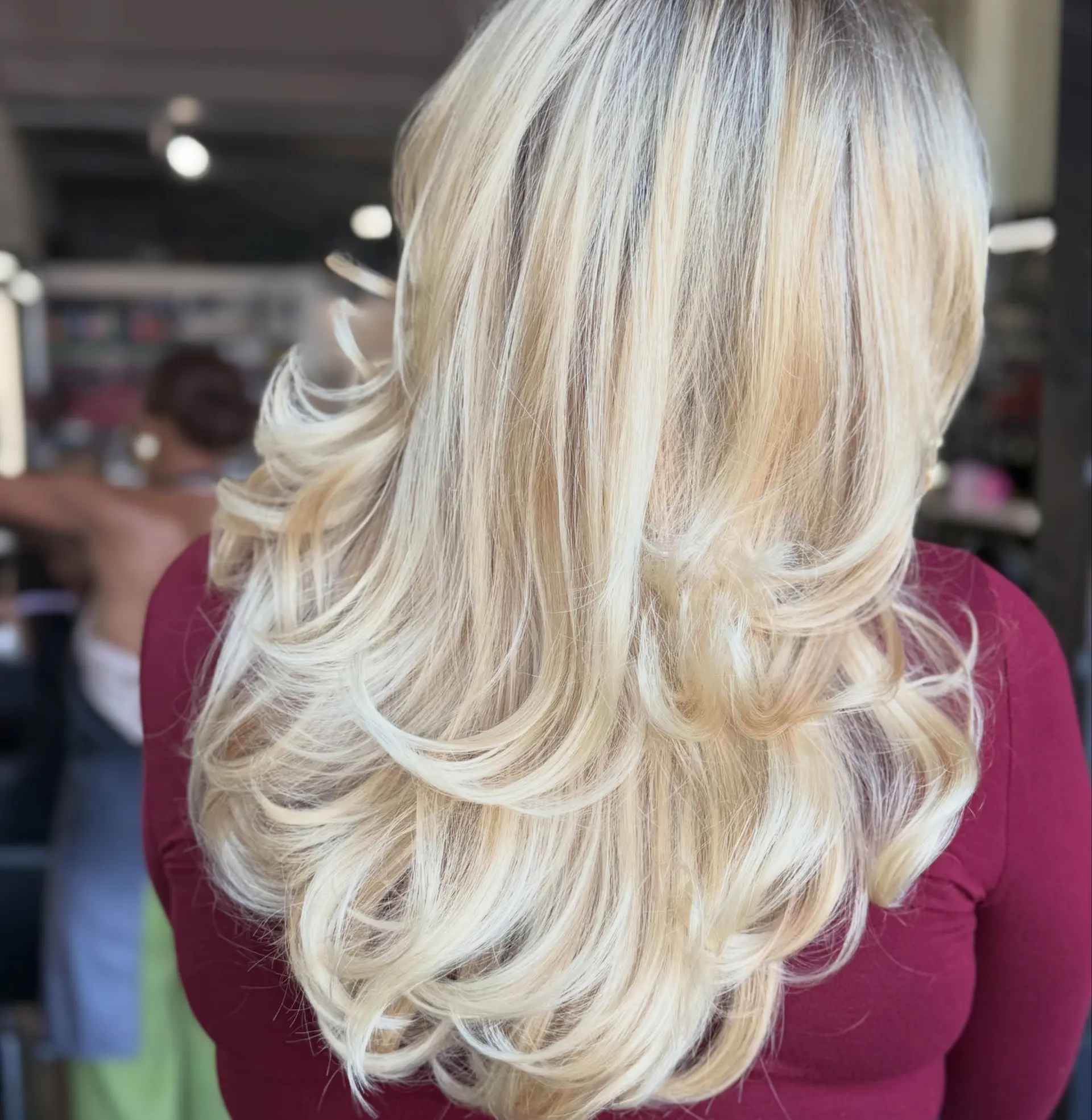 A voluminous, bouncy blowout on long blonde hair with feathered layers and flipped ends. 1