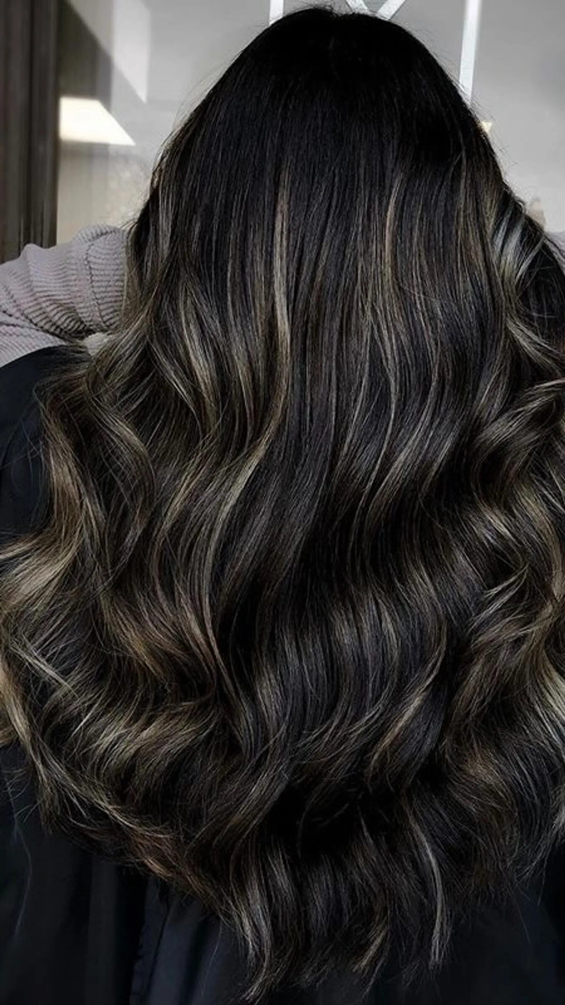 Long dark brunette hair cut with flowing layers and enhanced with subtle dimensional highlights, styled into soft waves. 1