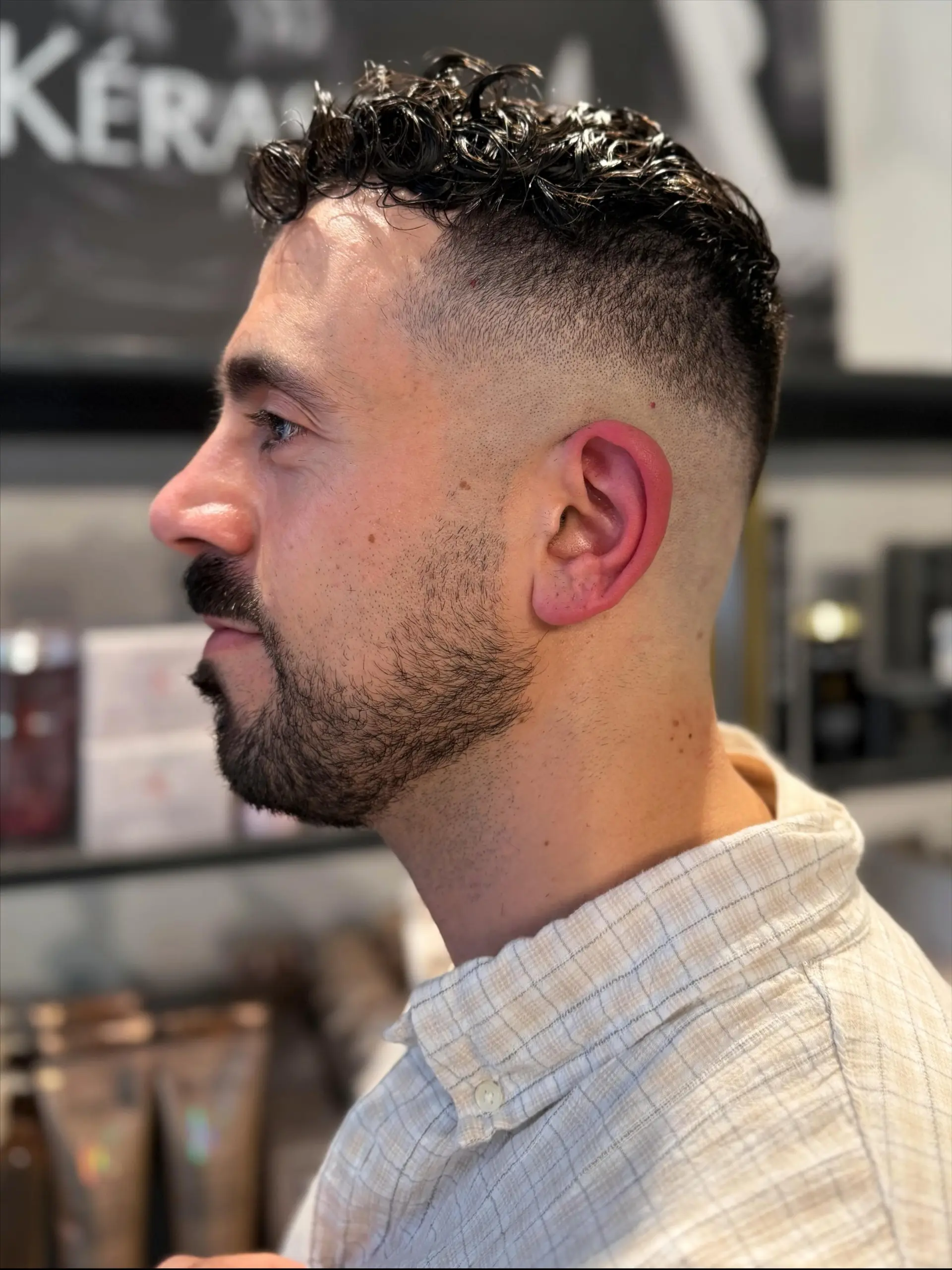 A tight high skin fade cut with natural defined curls on top and a neatly groomed beard. 1