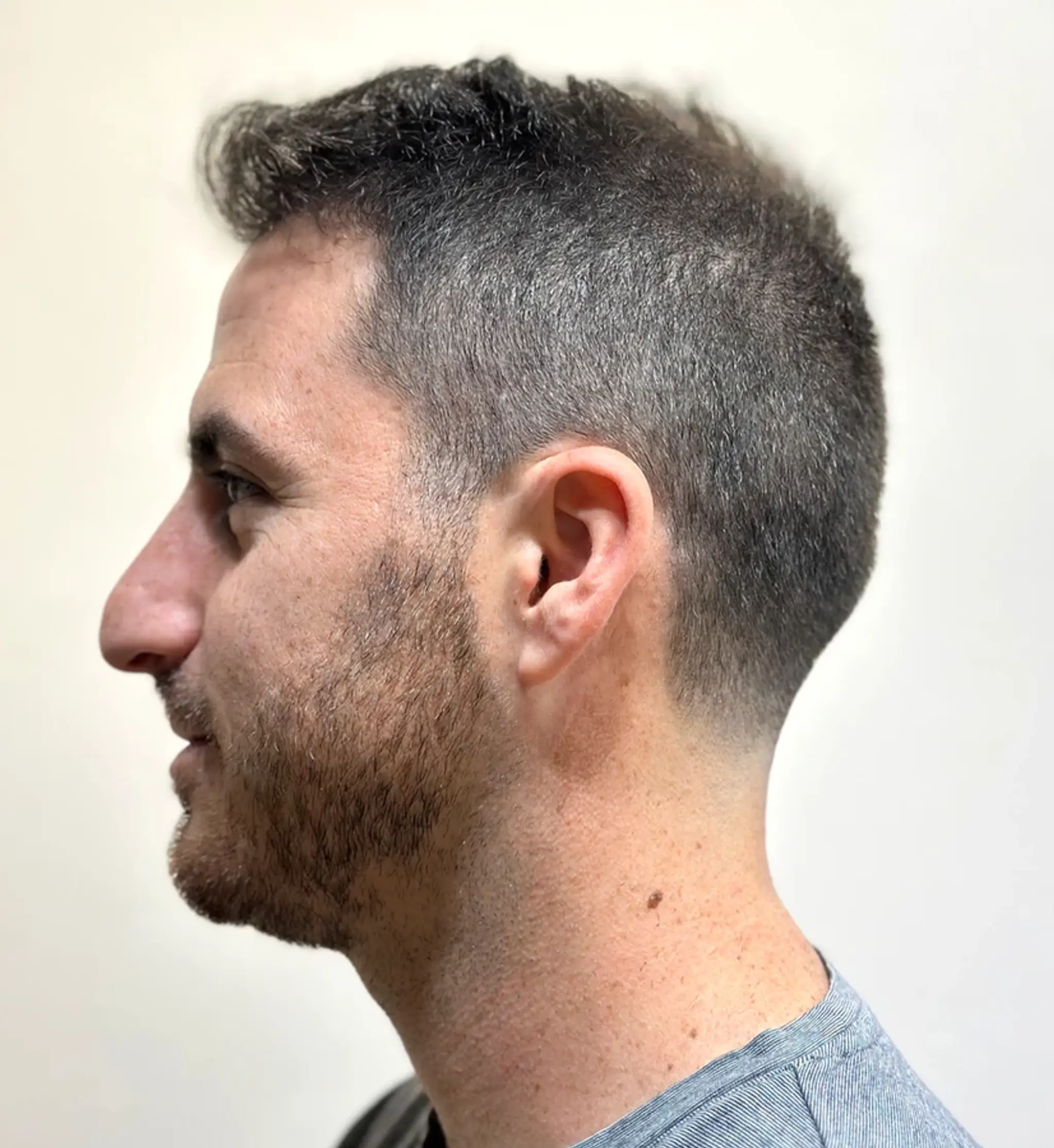 A modern fade with a tapered precision, this clean cut features a side part and detailed edge work, blending dark brown hues with subtle gray transitions.