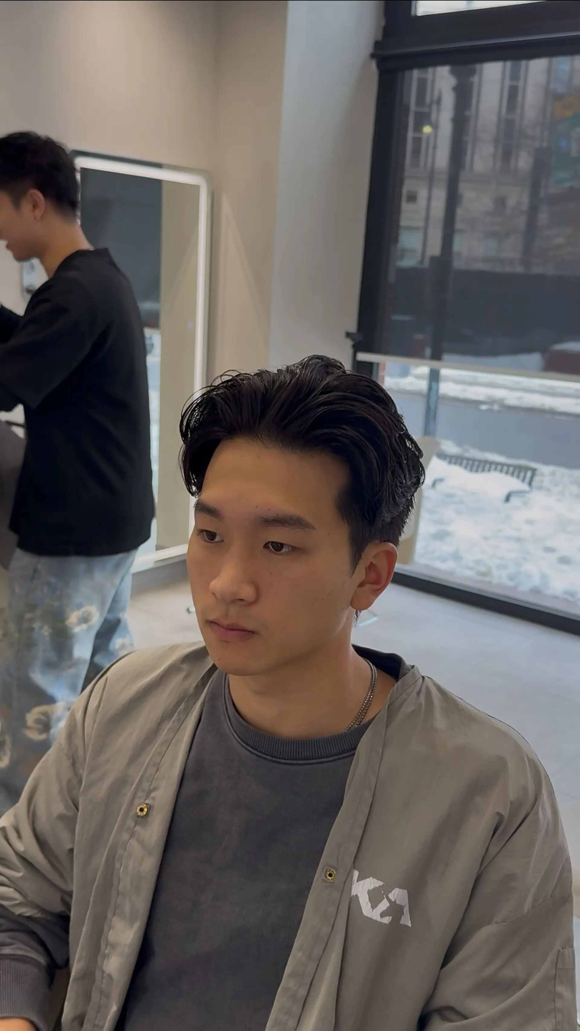 A men's center-parted textured haircut styled with soft volume and waves sweeping back from the forehead. 1