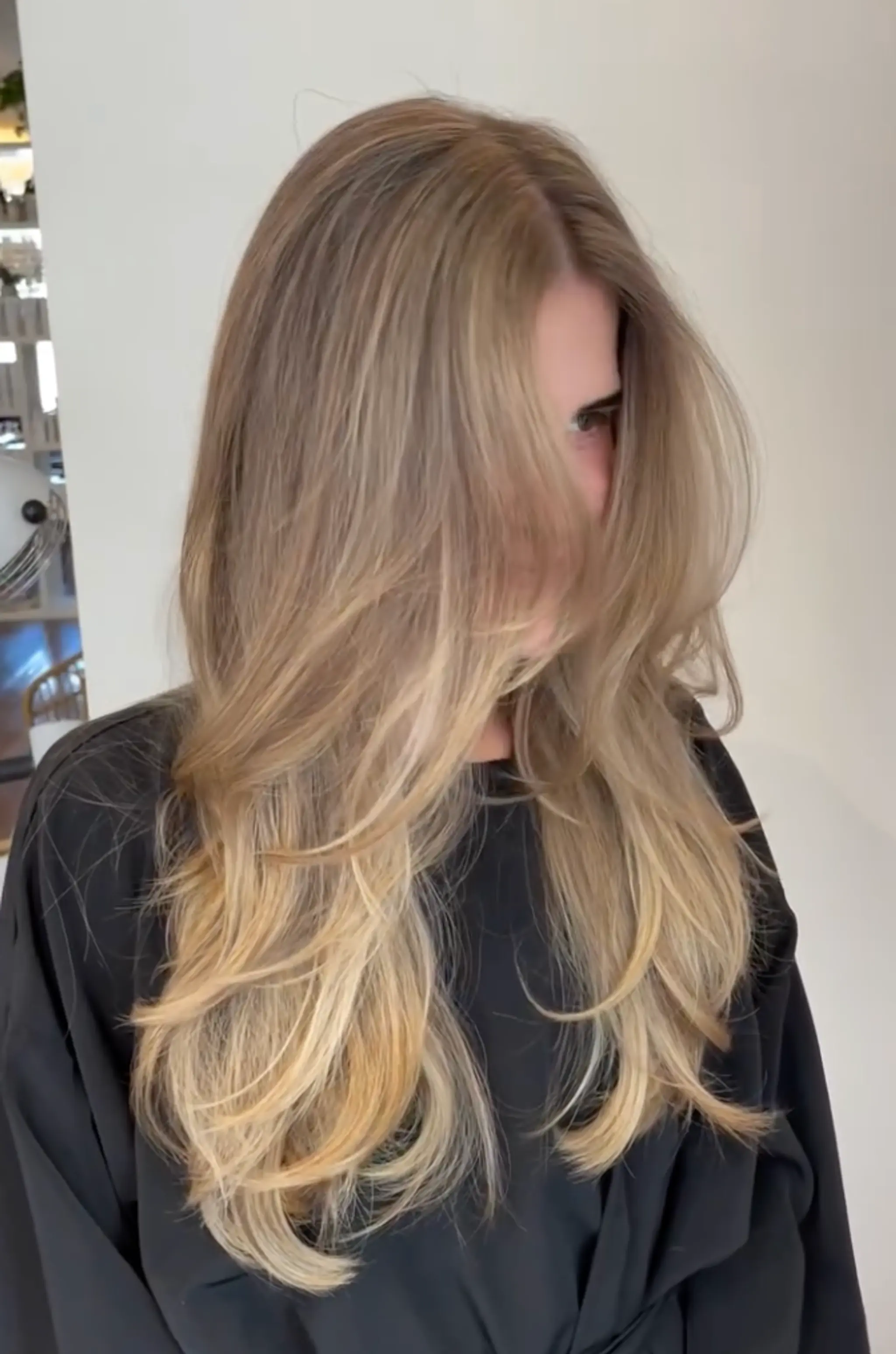 Long, wavy hair with a layered cut and a side part, featuring a natural blend of blonde and light brown shades.