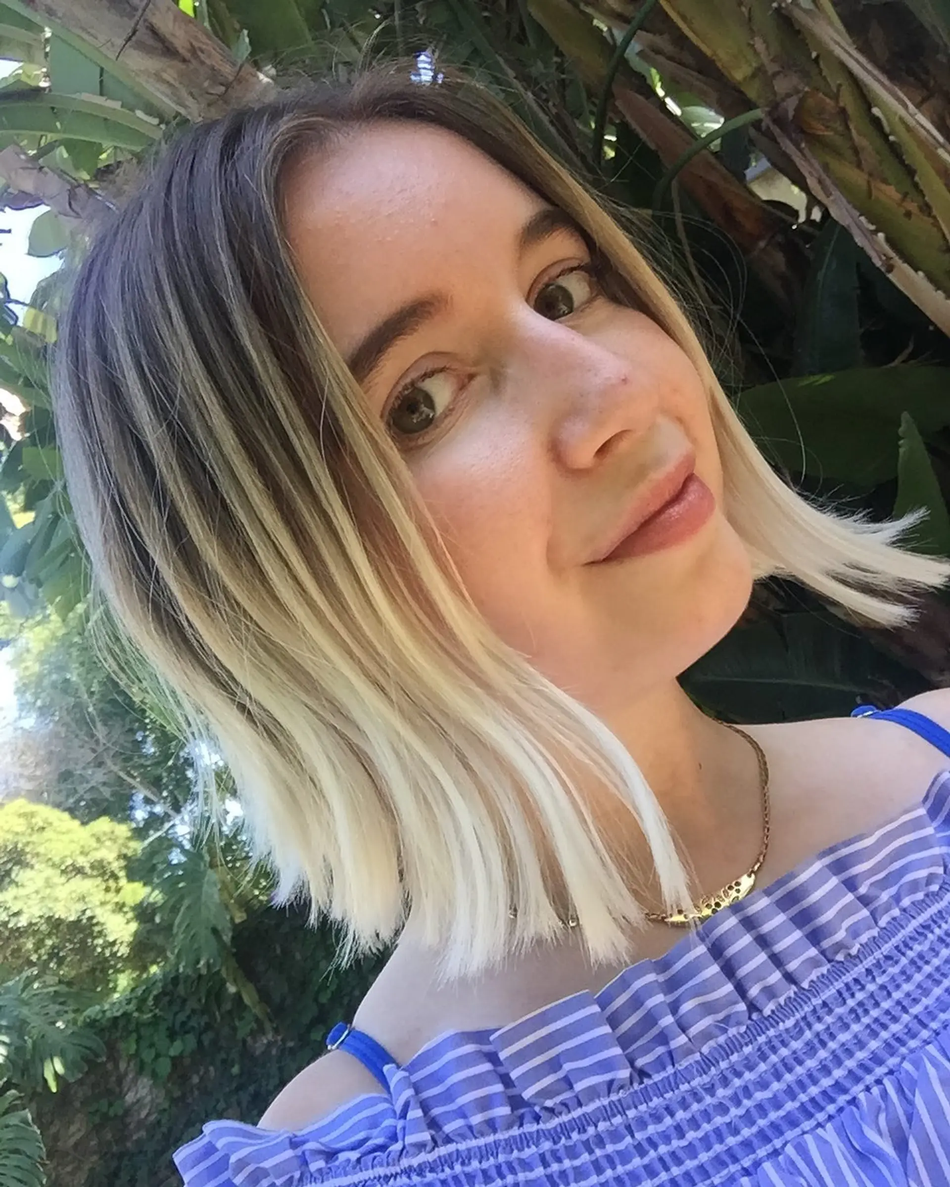 A chin-length blunt bob featuring platinum blonde ends with a dark brown shadow root and center part. 1