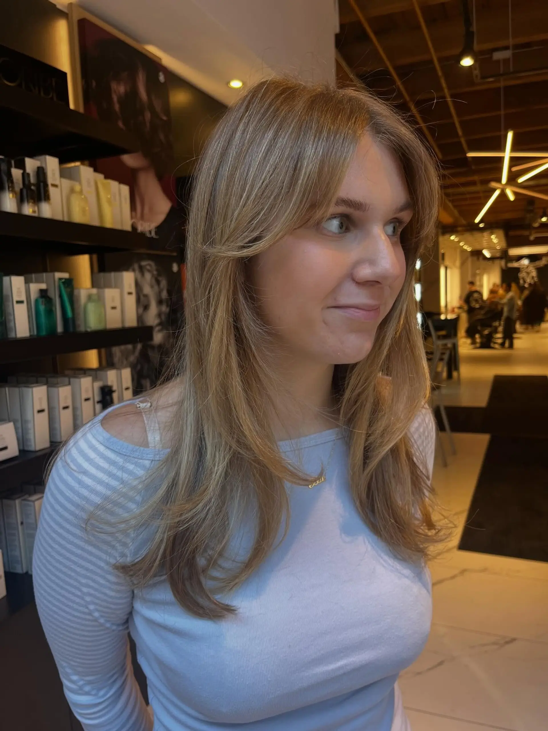 Long ash blonde hair featuring textured face-framing layers and parted curtain bangs styled in a soft, smooth blowout with gently curved ends. 1