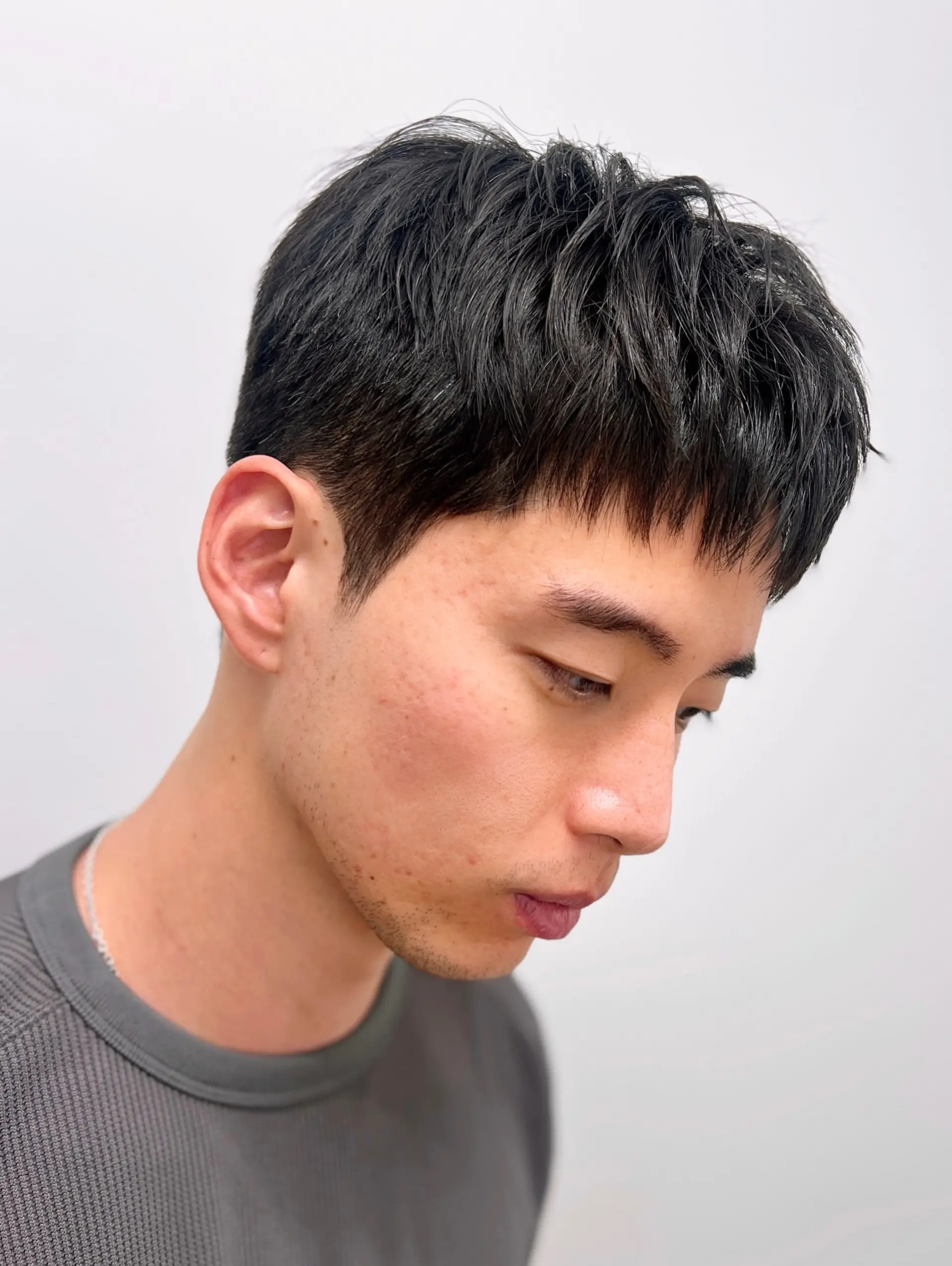 A modern short haircut featuring a textured crop on top, choppy forward fringe, and cleanly flattened sides achieved with a down perm. 1