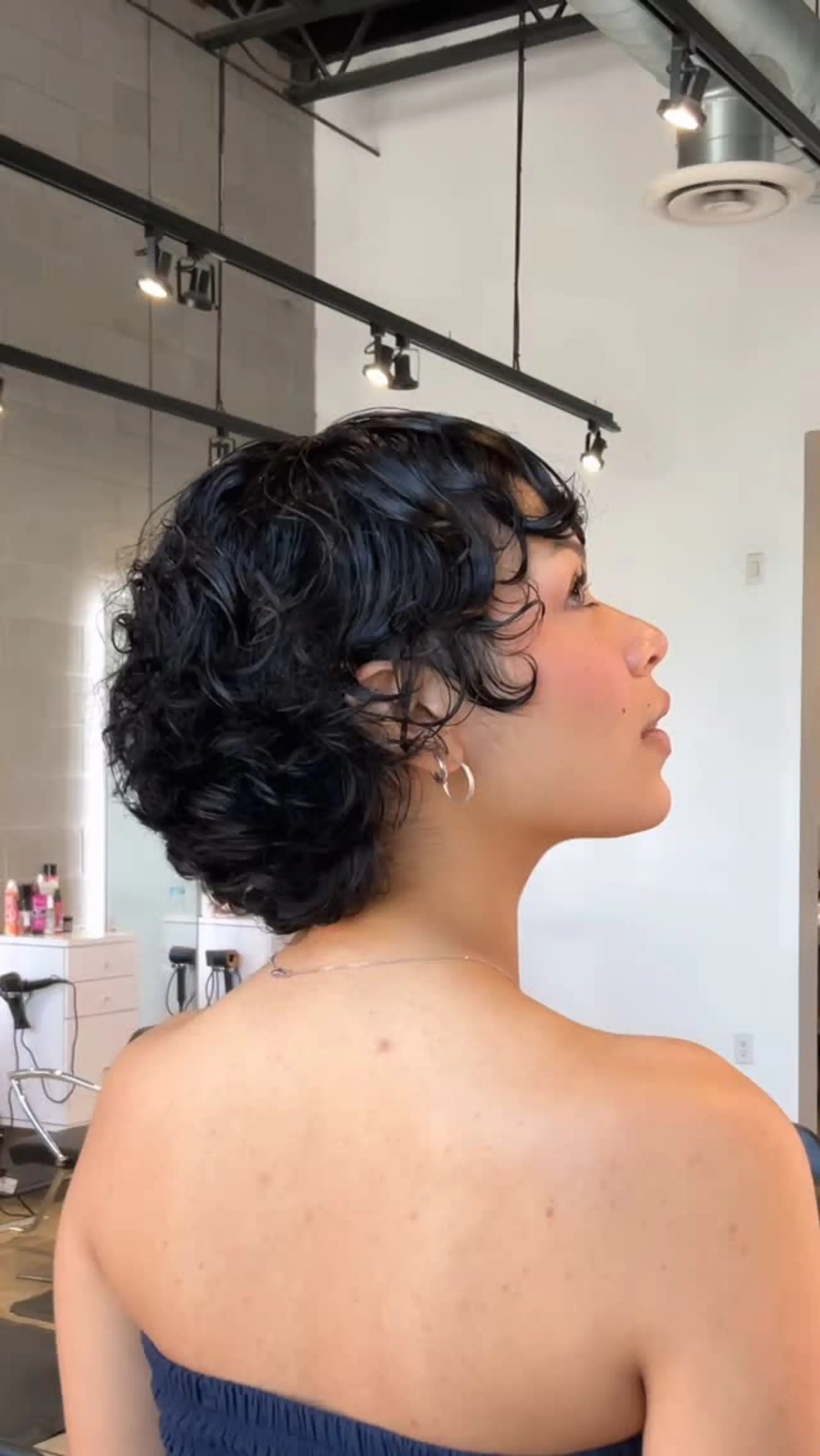 A textured short curly bixie cut with soft tendrils framing the face and full body tapering at the nape. 1