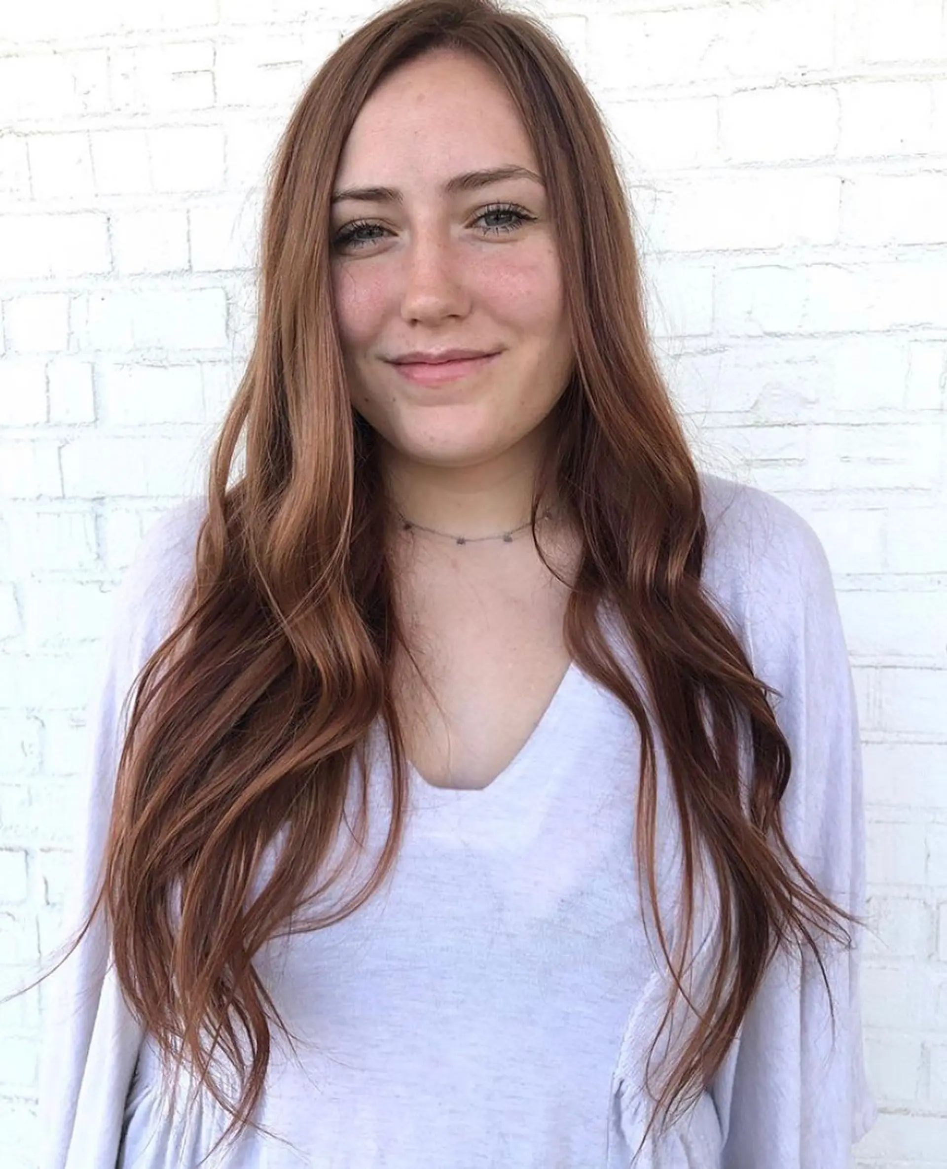 Long, shiny auburn hair parted in the middle and styled with soft, cascading waves. 1