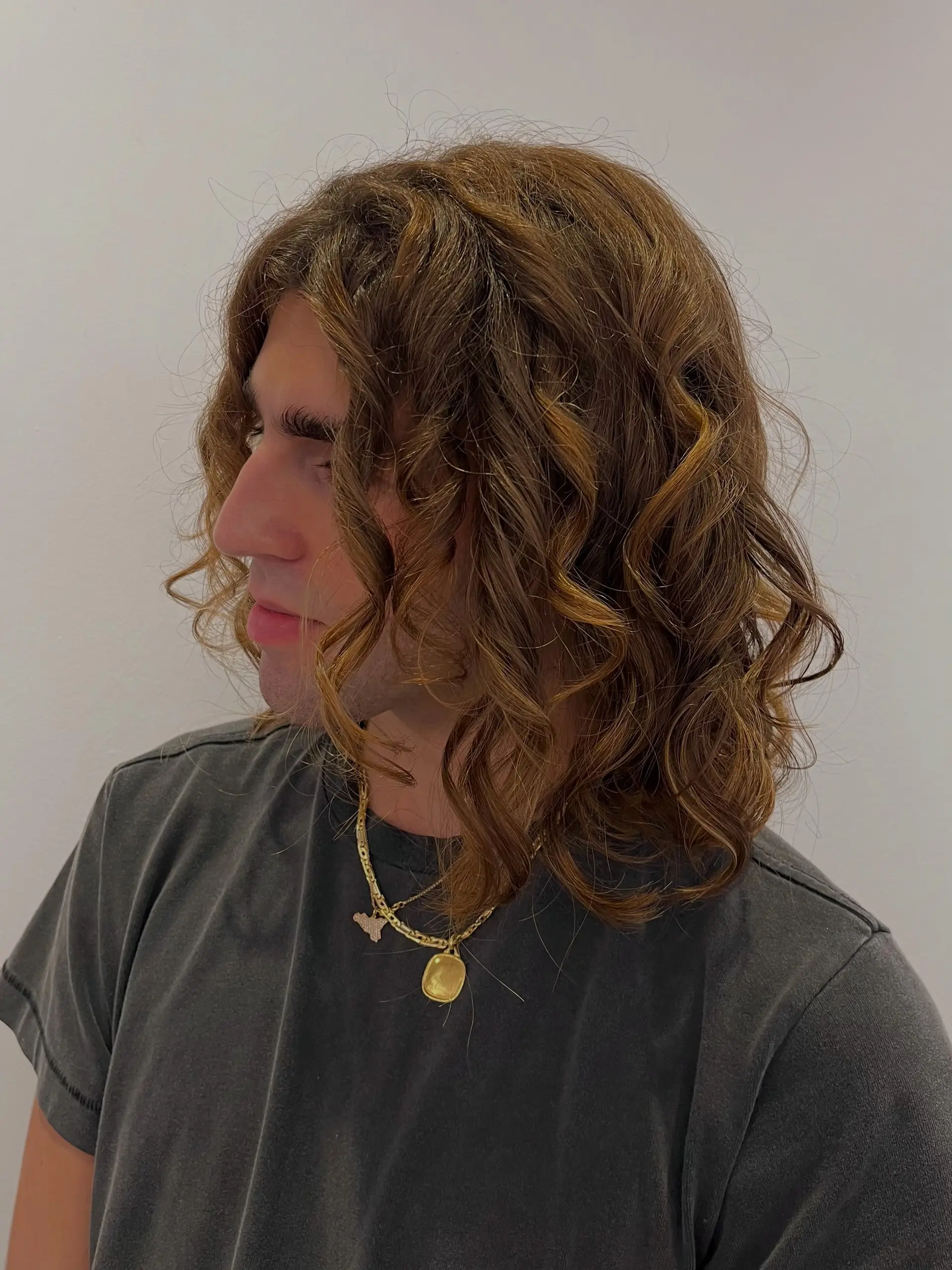 Medium-length layered haircut shaped to enhance natural bouncy curls with defined ringlets and warm golden-brown undertones. 1