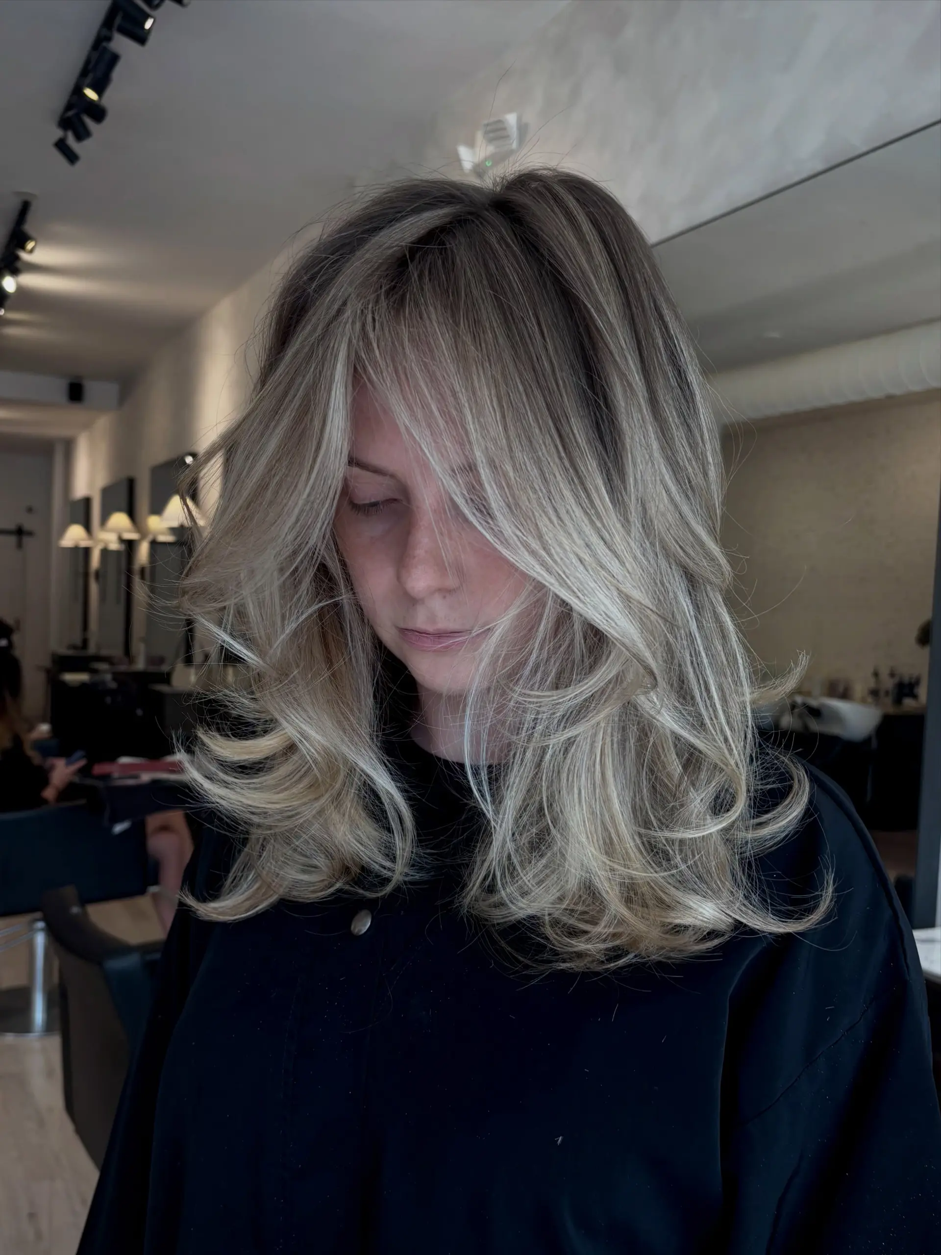 Medium-length layered blonde hair styled with voluminous, outward-flipped blowout curls and face-framing curtain bangs. 1
