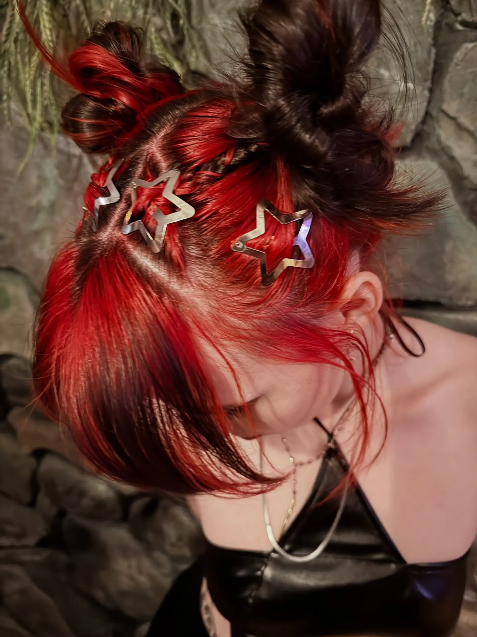 Playful space buns styled with accent braids and silver star clips over vivid crimson red hair. 1