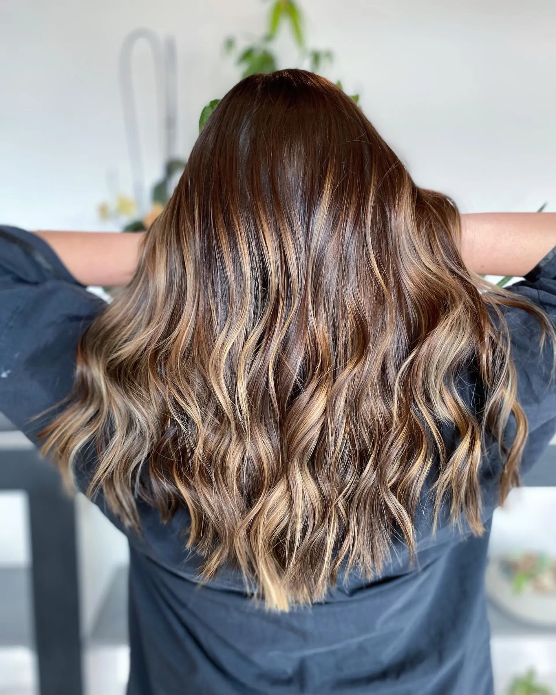 Long dimensional brunette hair enhanced with warm caramel balayage highlights and styled in soft, textured waves. 1