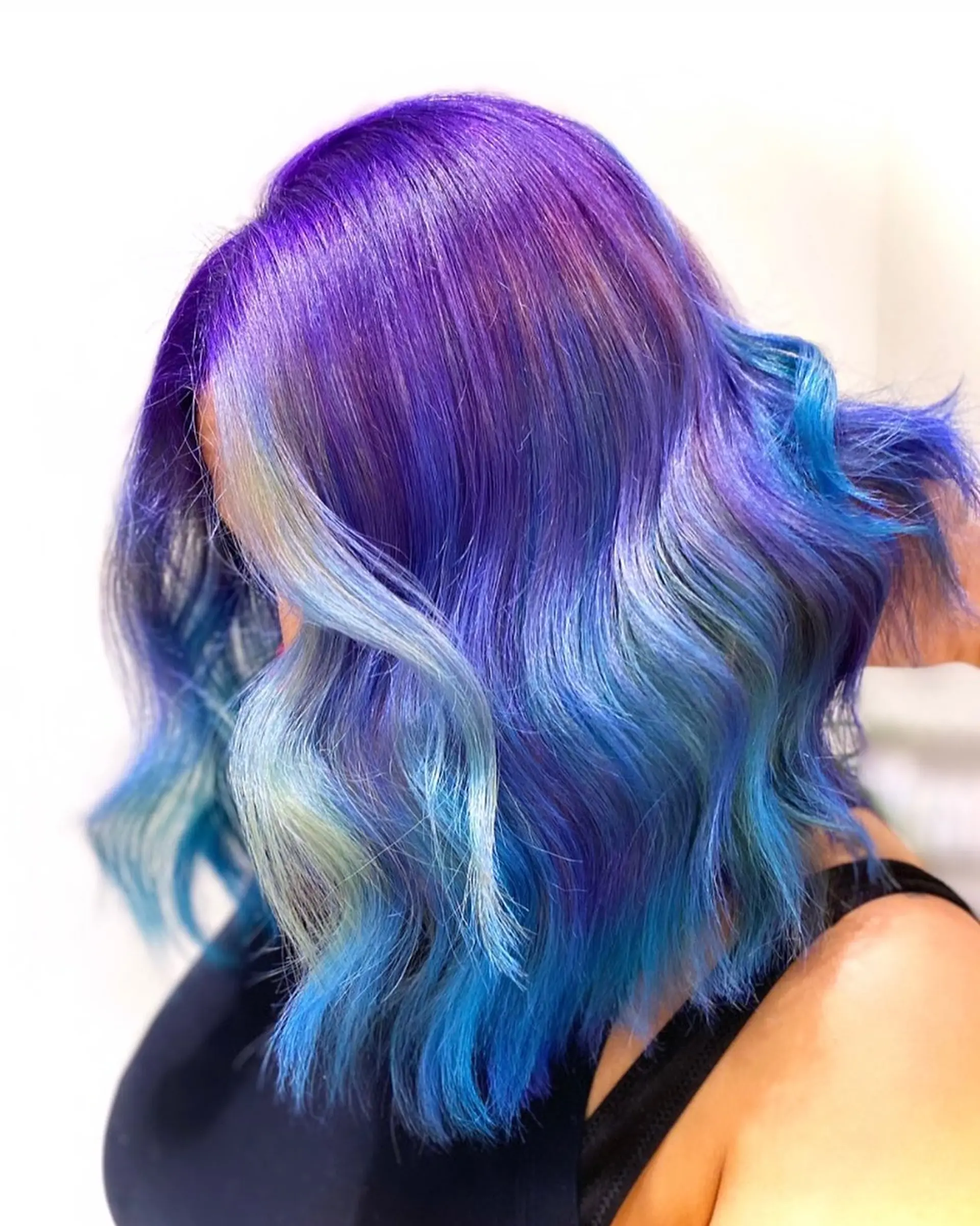 Medium-length wavy hair with a vibrant gradation of violet, blue, and turquoise colors, styled with beachy waves for added texture and movement. 1
