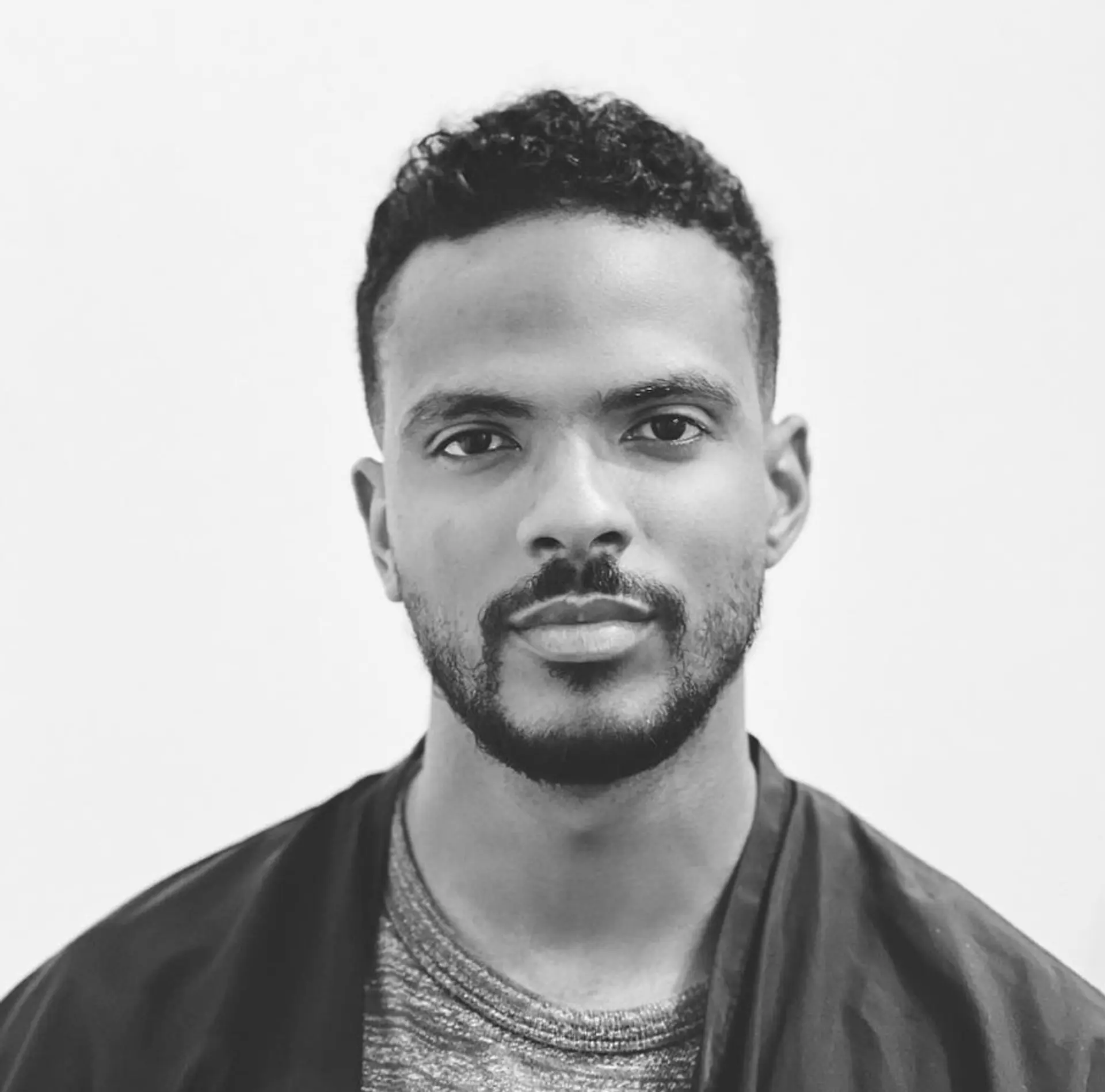 A neat taper fade on the sides and back, blending into short, tightly defined curls on top. The curls are neatly trimmed for a sharp, clean look. 1