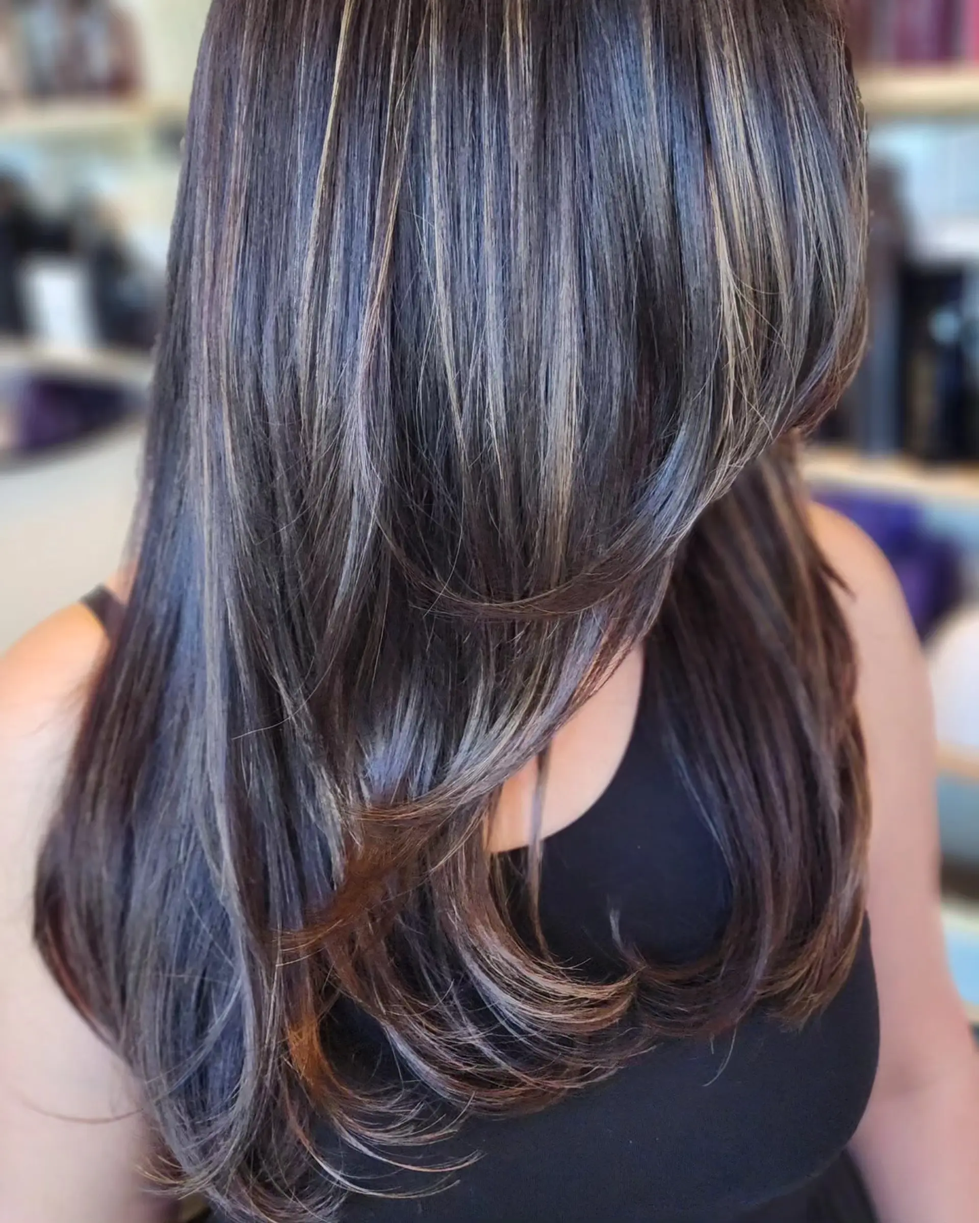 Long layered dark brown hair with delicate highlights, curtain bangs, and a soft bouncy blowout curled inward at the ends. 1