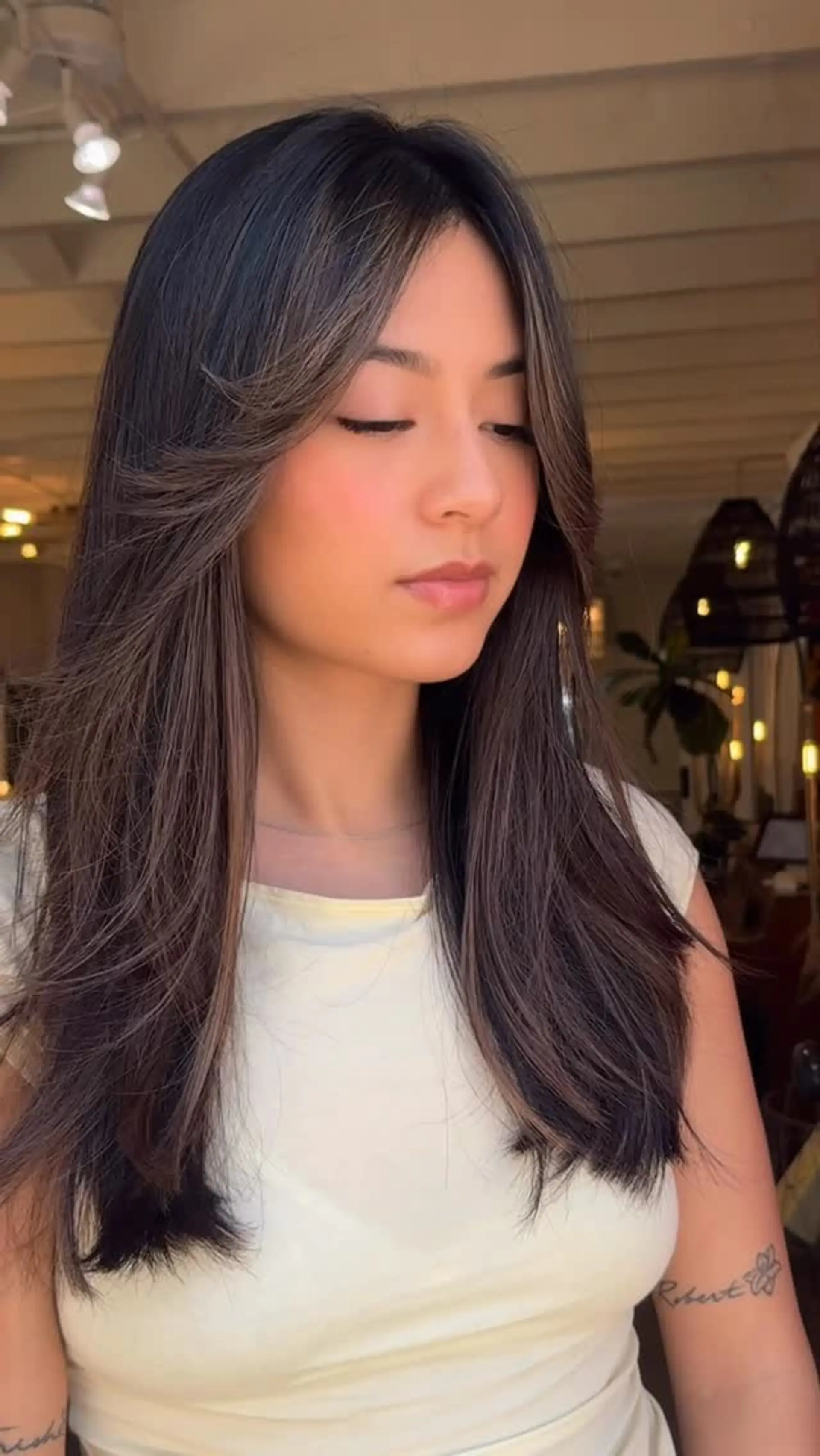 Long dark brunette hair featuring face-framing feathered layers and swept-out curtain bangs. 1