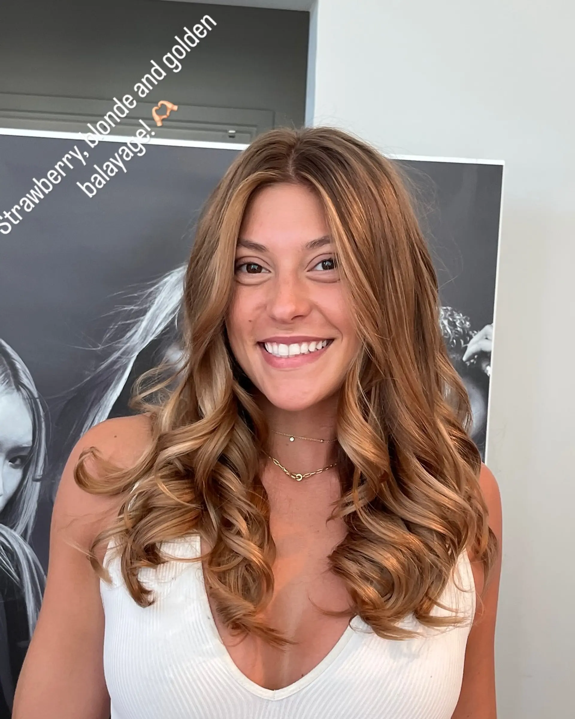A medium-length wavy hairstyle with a dimensional strawberry blonde balayage and soft curls. 1