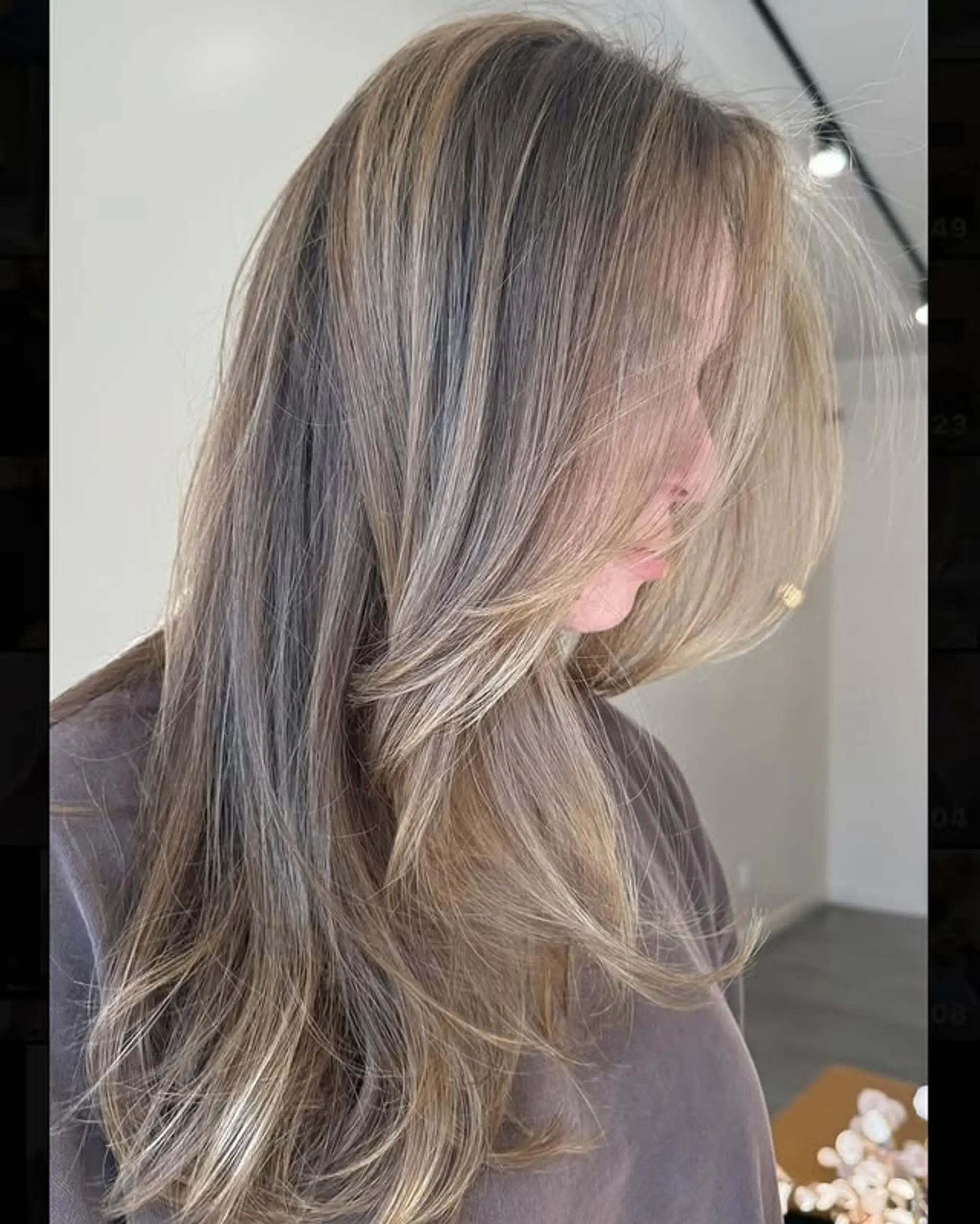 A long, layered hairstyle with a mix of brown and blonde hues creating a bronde balayage effect. Gentle waves enhance the texture. 1