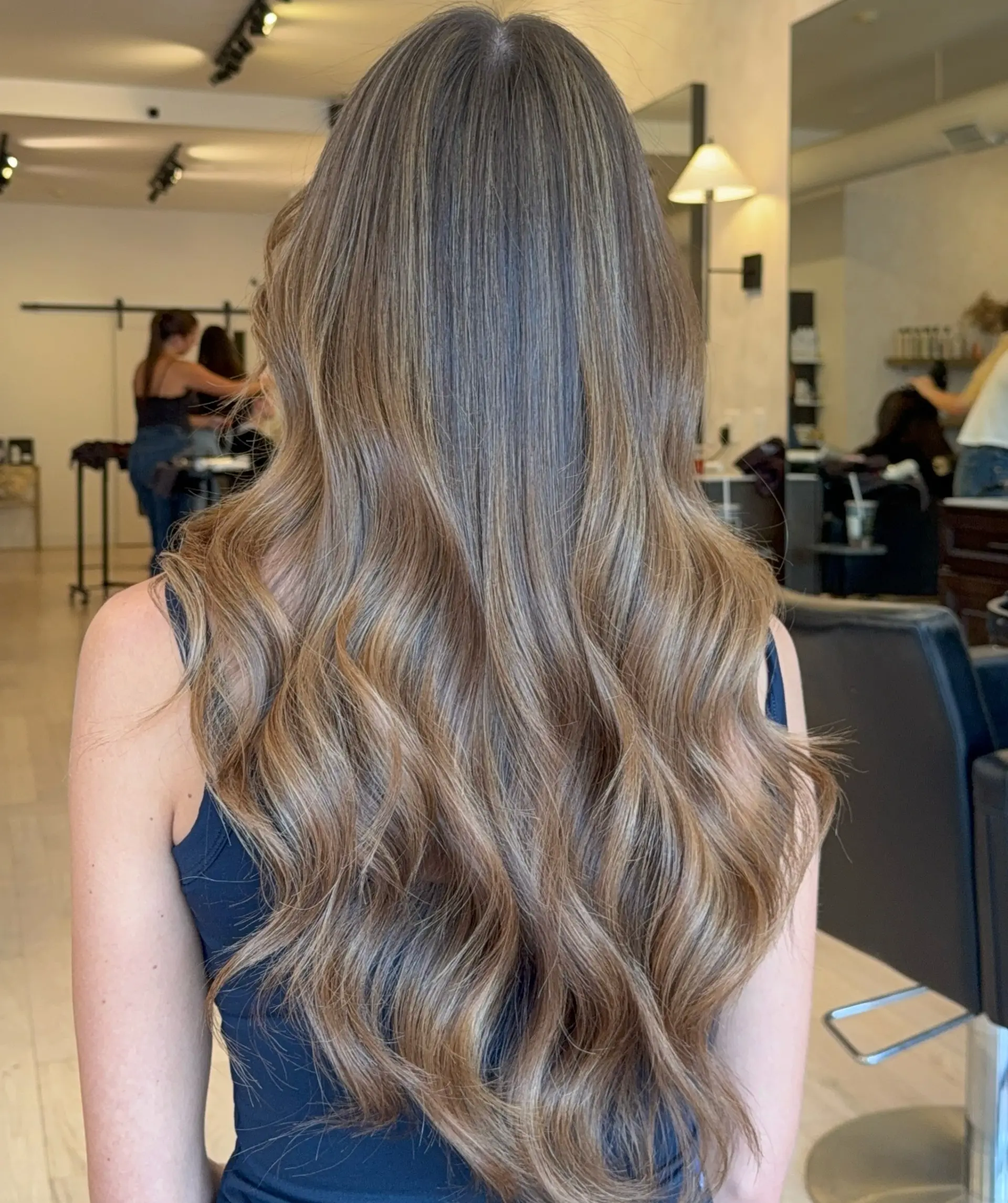 Long dimensional brunette hair with seamlessly blended lighter tones, styled in soft, loose cascading waves. 1