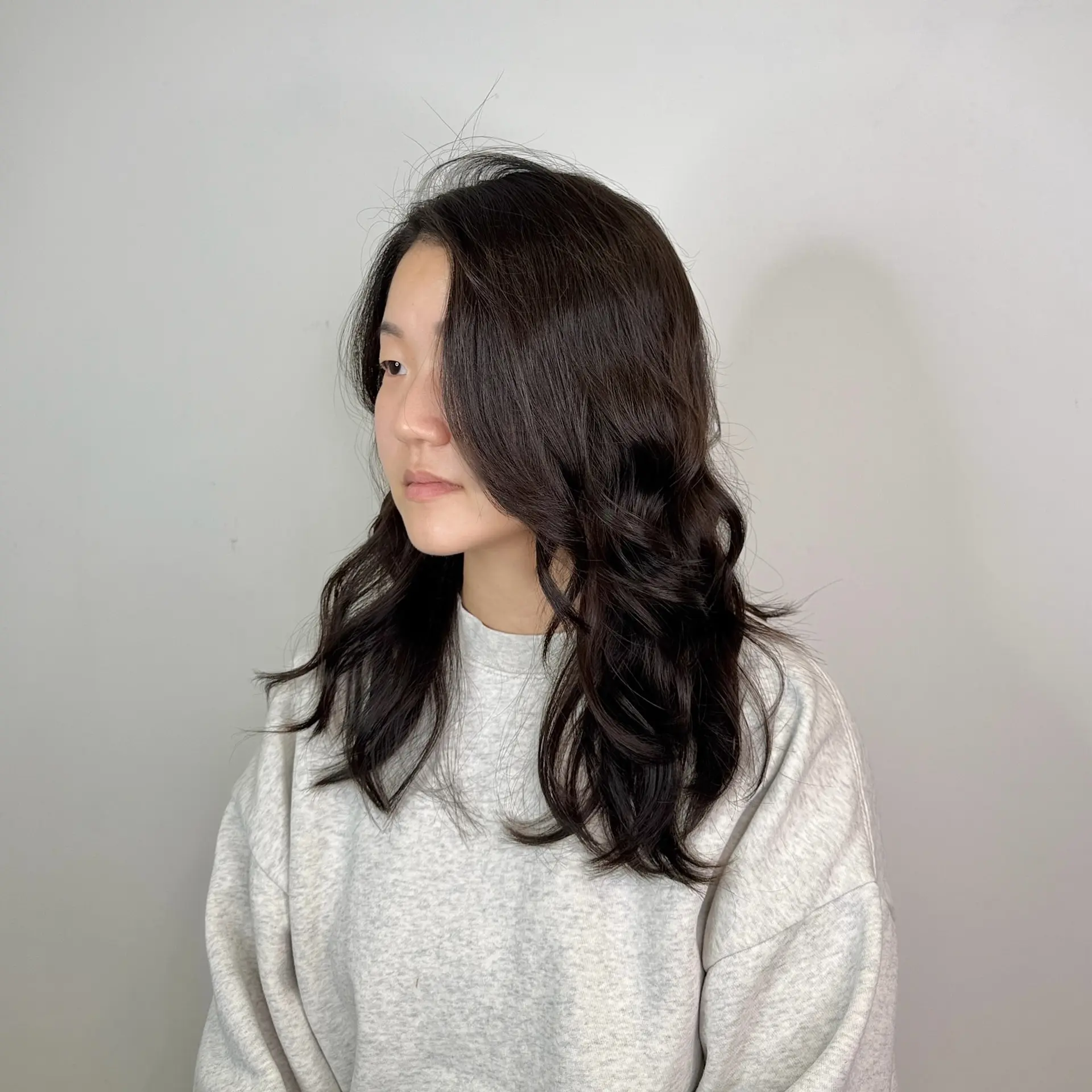 Medium-length dark hair styled with soft, voluminous body waves and a sweeping side-parted front fringe. 1