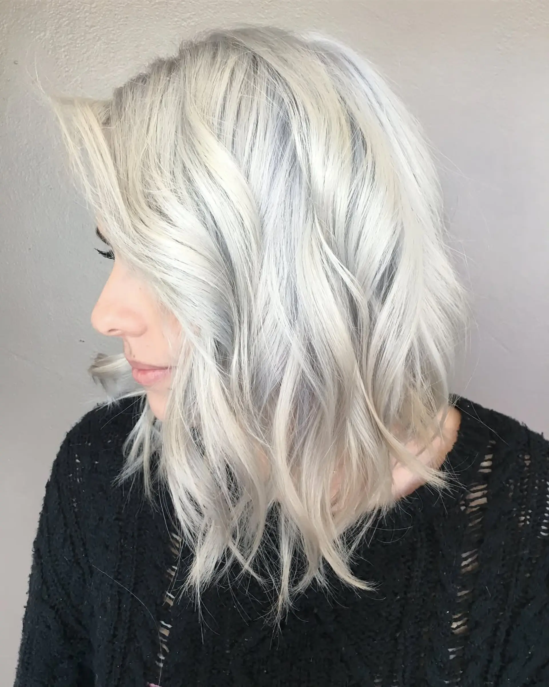 A textured shoulder-length lob styled in soft, undone waves with a striking icy platinum ash blonde color. 1