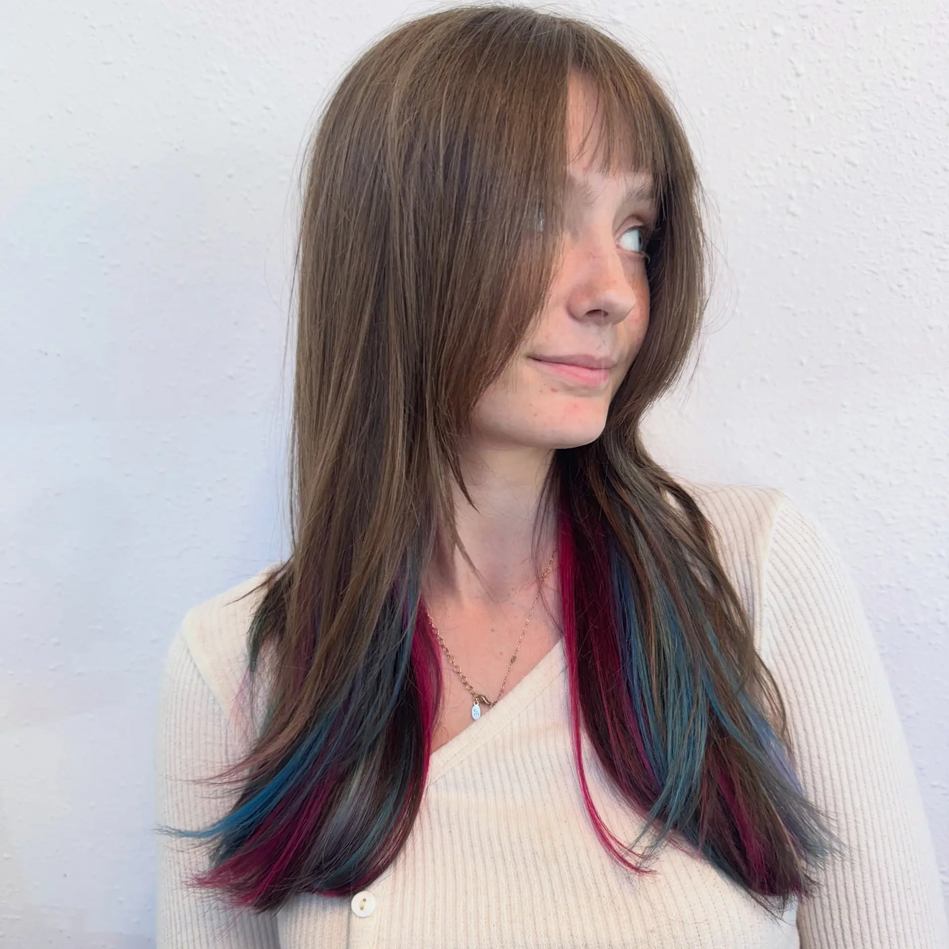 Straight long brunette hair with front bangs and face-framing layers, revealing vibrant magenta and blue peekaboo color beneath. 1