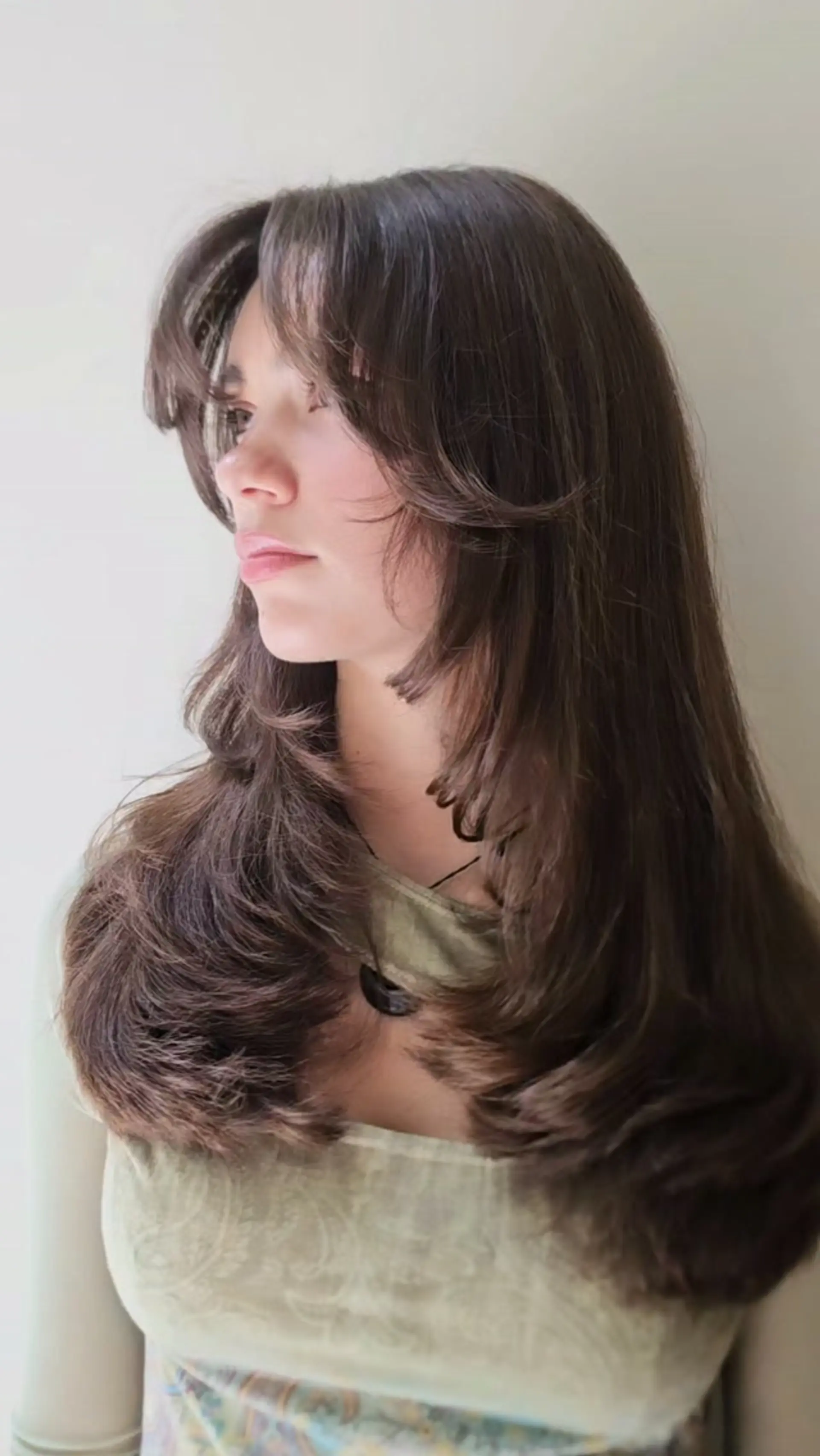 Long brown layered haircut featuring soft curtain bangs and bouncy, face-framing rounded layers. 1