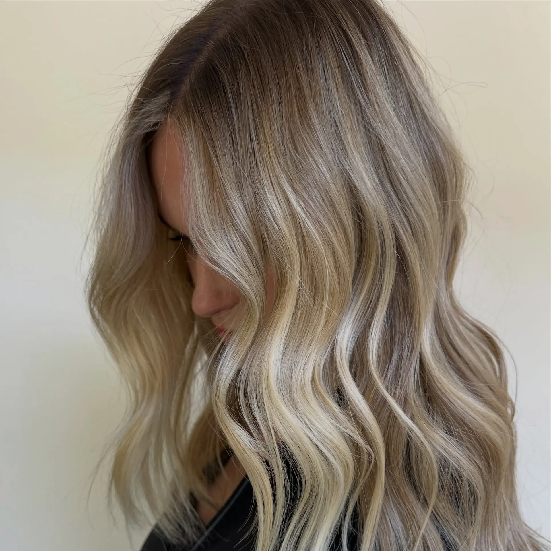 A dimensional lived-in blonde balayage styled into soft, flowing beach waves with a seamless root melt. 1