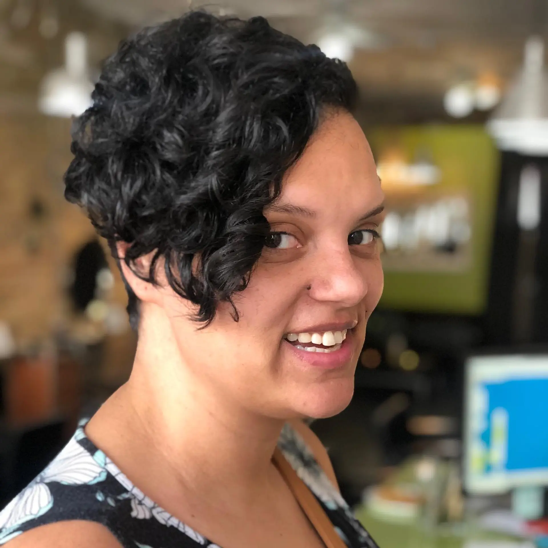 A short, curly undercut pixie haircut with defined curls swept forward across the front. 1