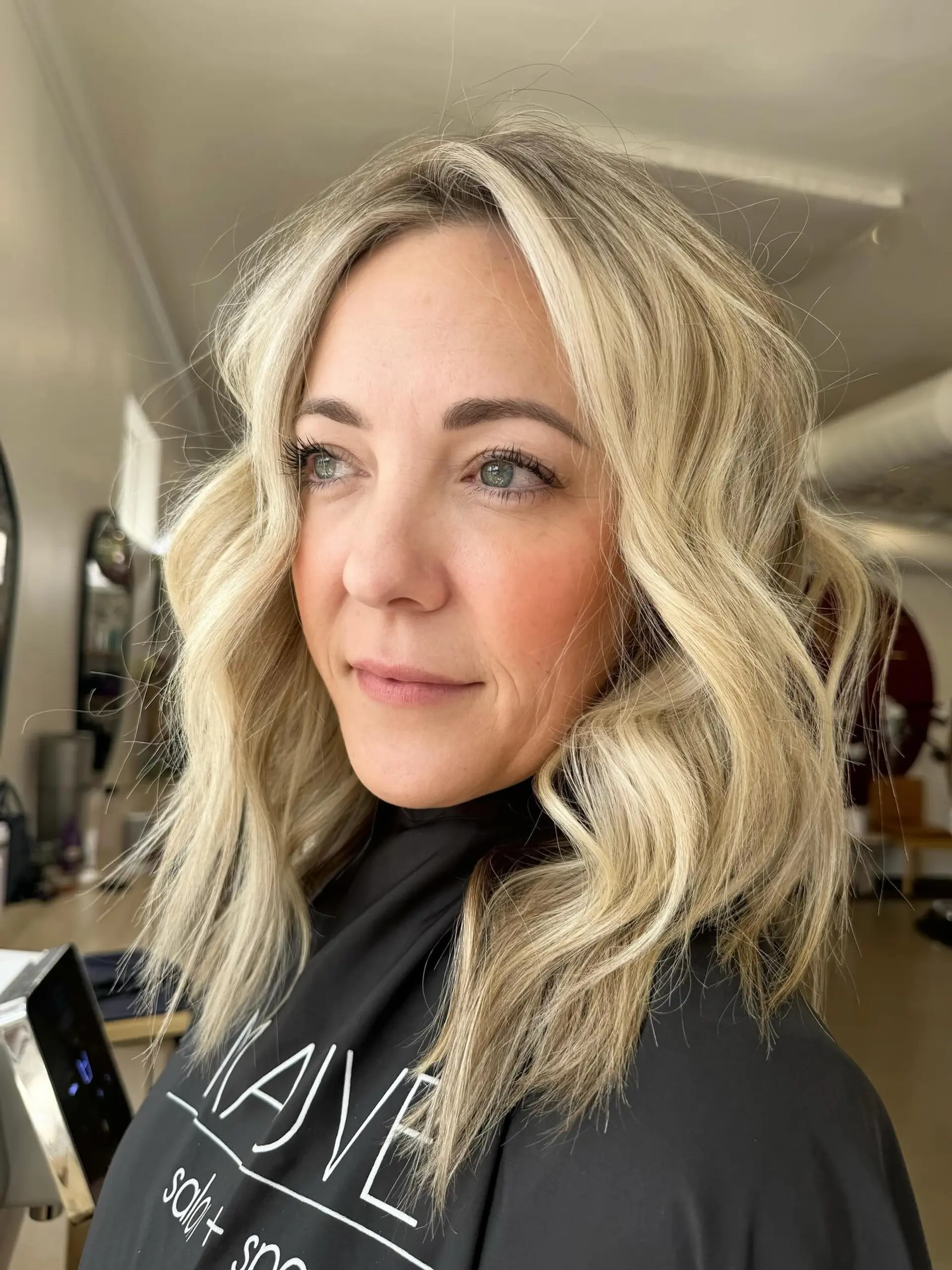 A medium-length textured lob styled in soft, lived-in waves featuring bright dimensional blonde tones. 1