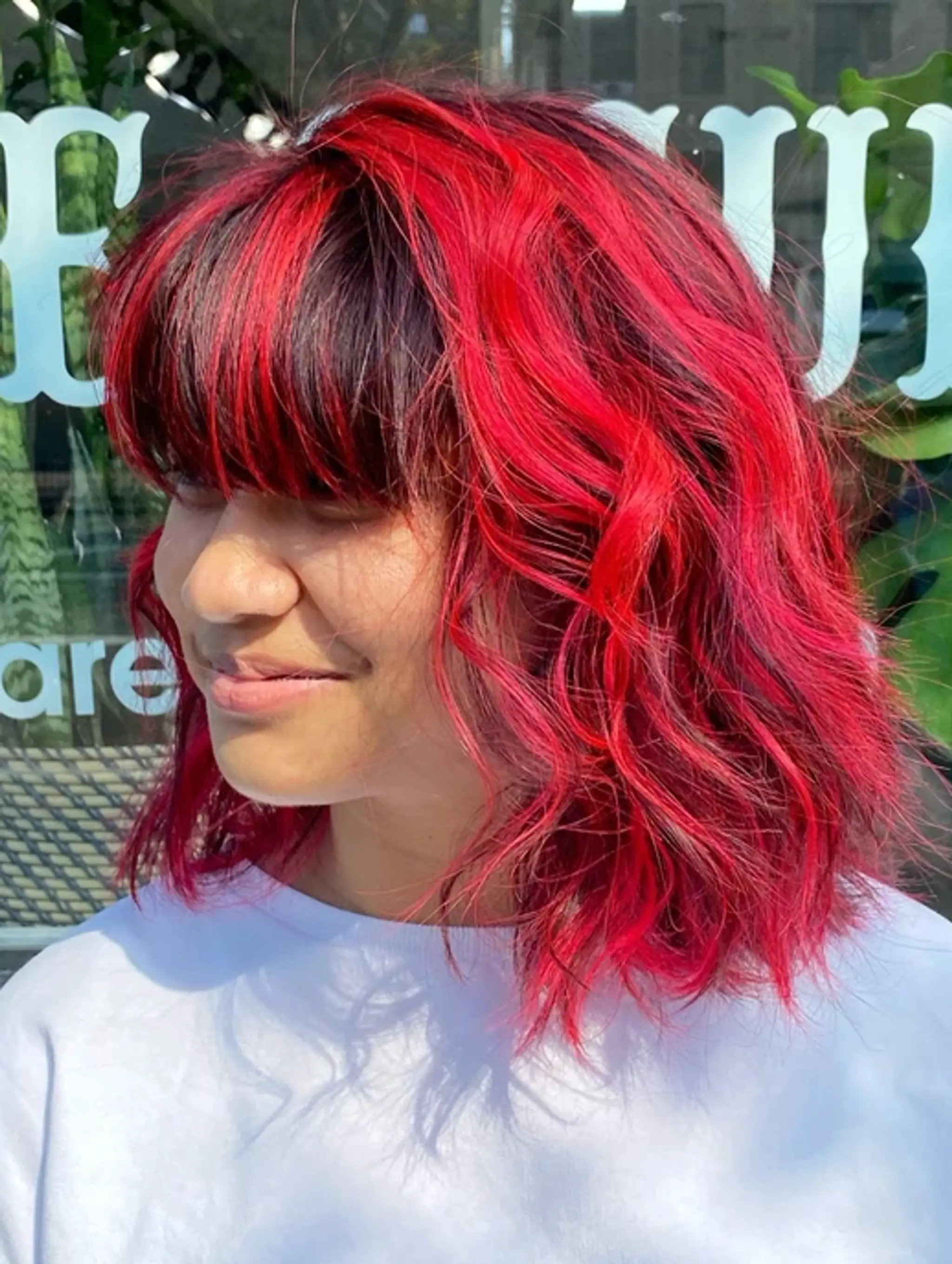 Medium-length wavy hair dyed in vibrant red with black undertones, layered waves, and a full thick fringe.